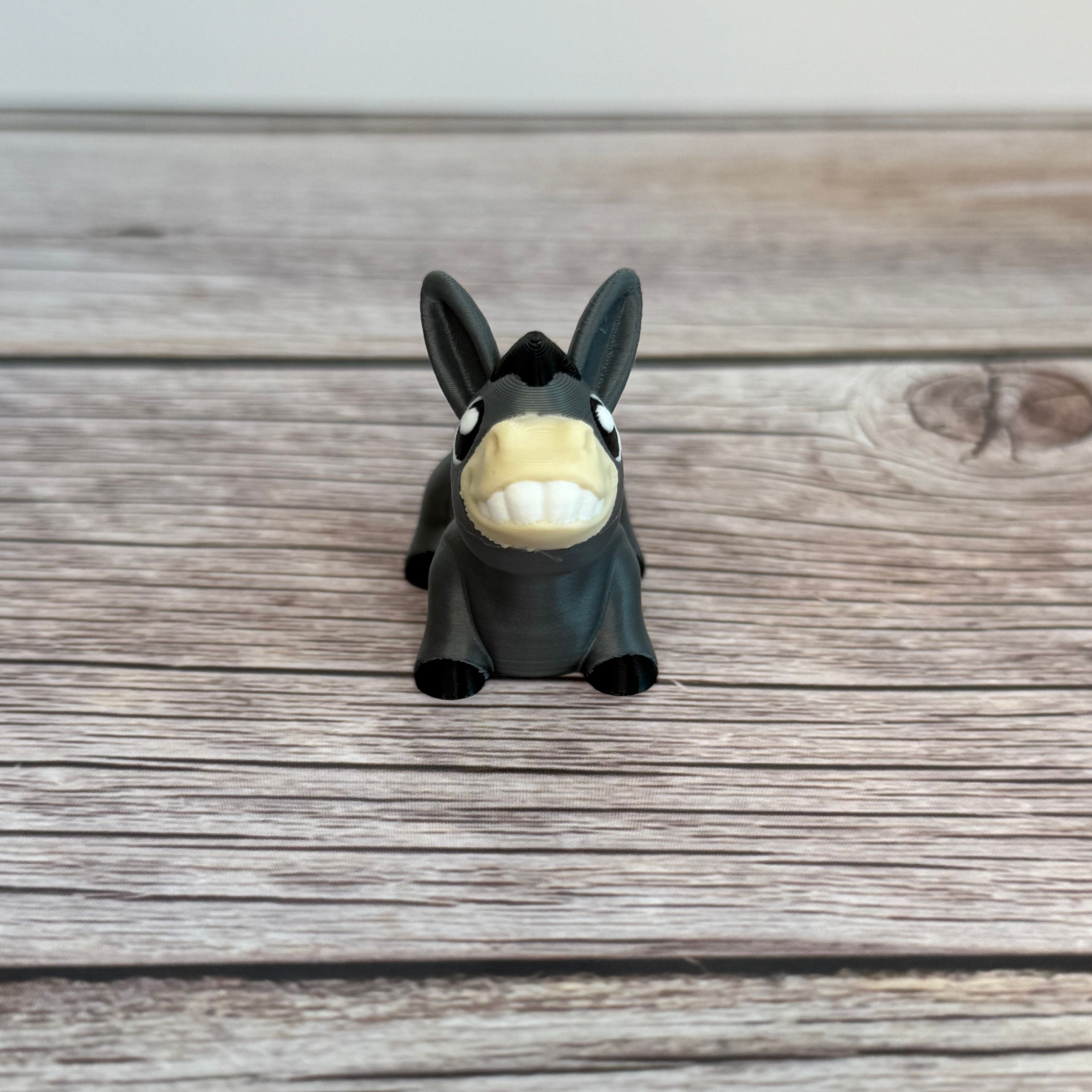 A small 3D printed gray donkey toy with movable segments, positioned on a wooden surface.