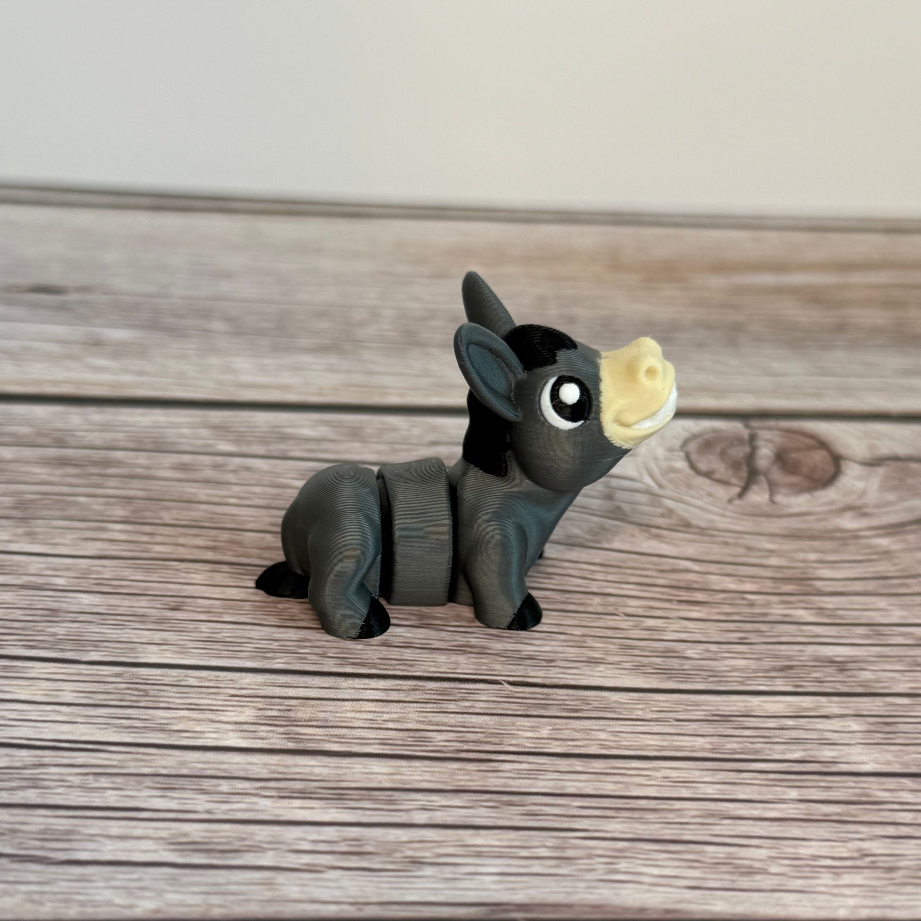 A small 3D printed gray donkey toy with movable segments, positioned on a wooden surface.