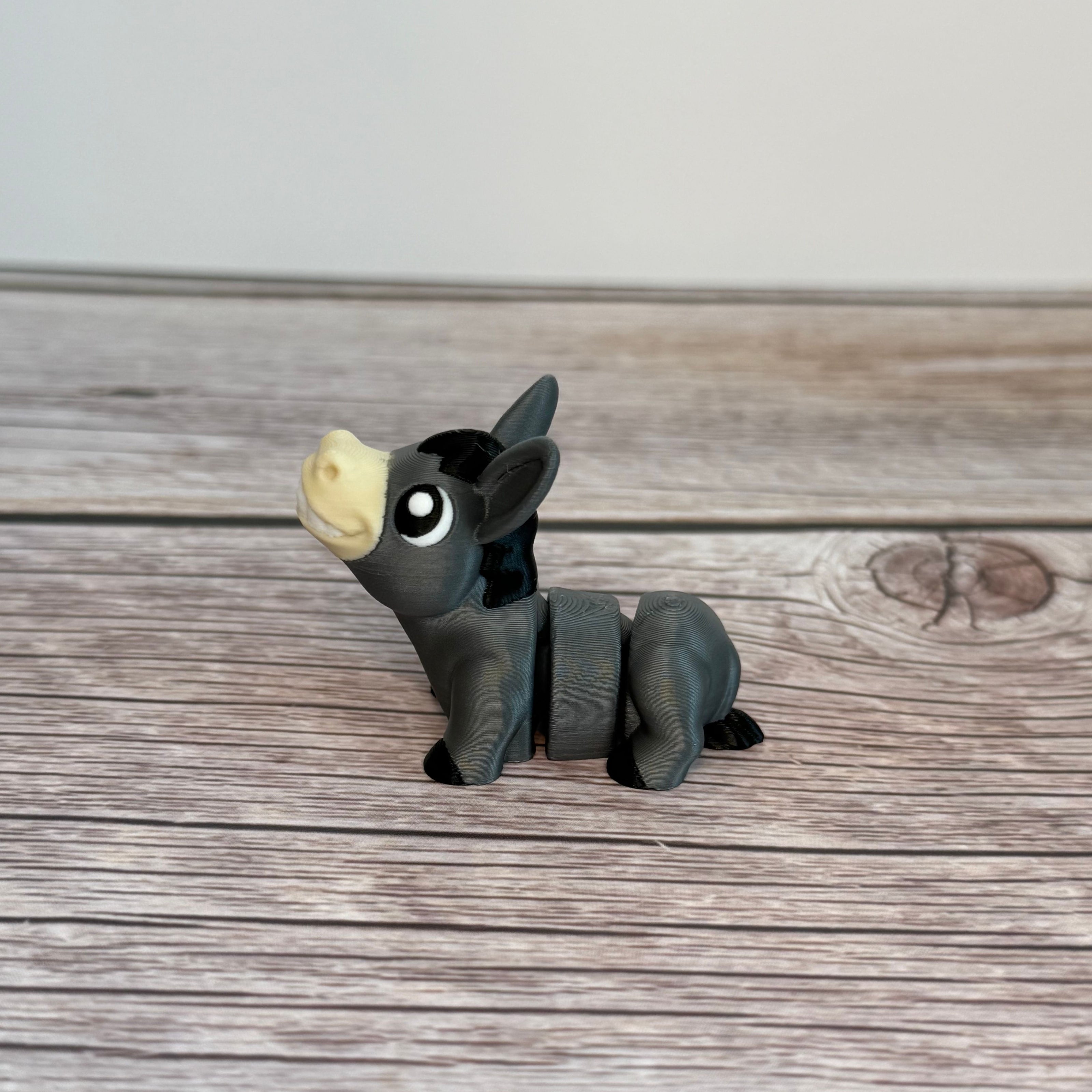 A small 3D printed gray donkey toy with movable segments, positioned on a wooden surface.
