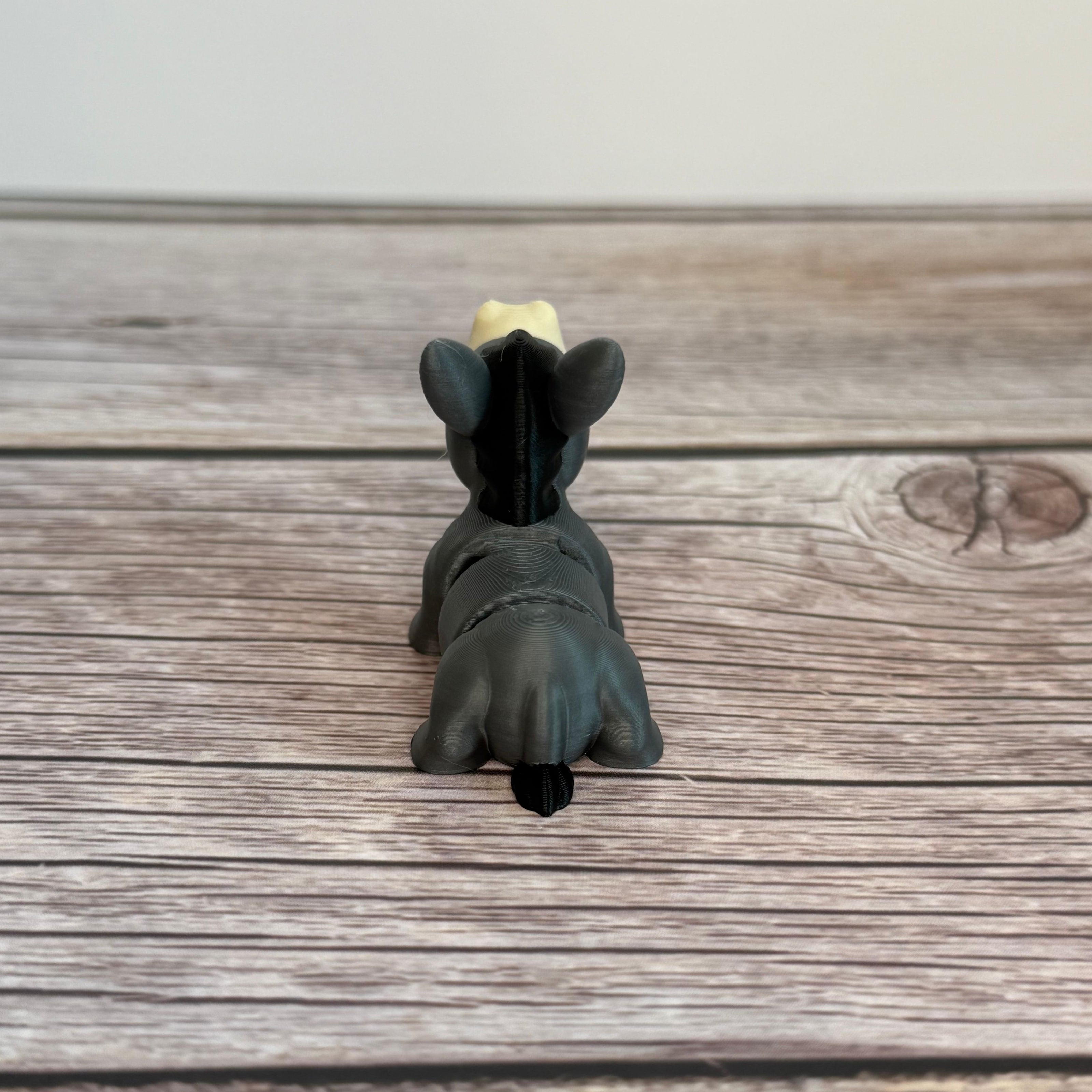 A small 3D printed gray donkey toy with movable segments, positioned on a wooden surface.