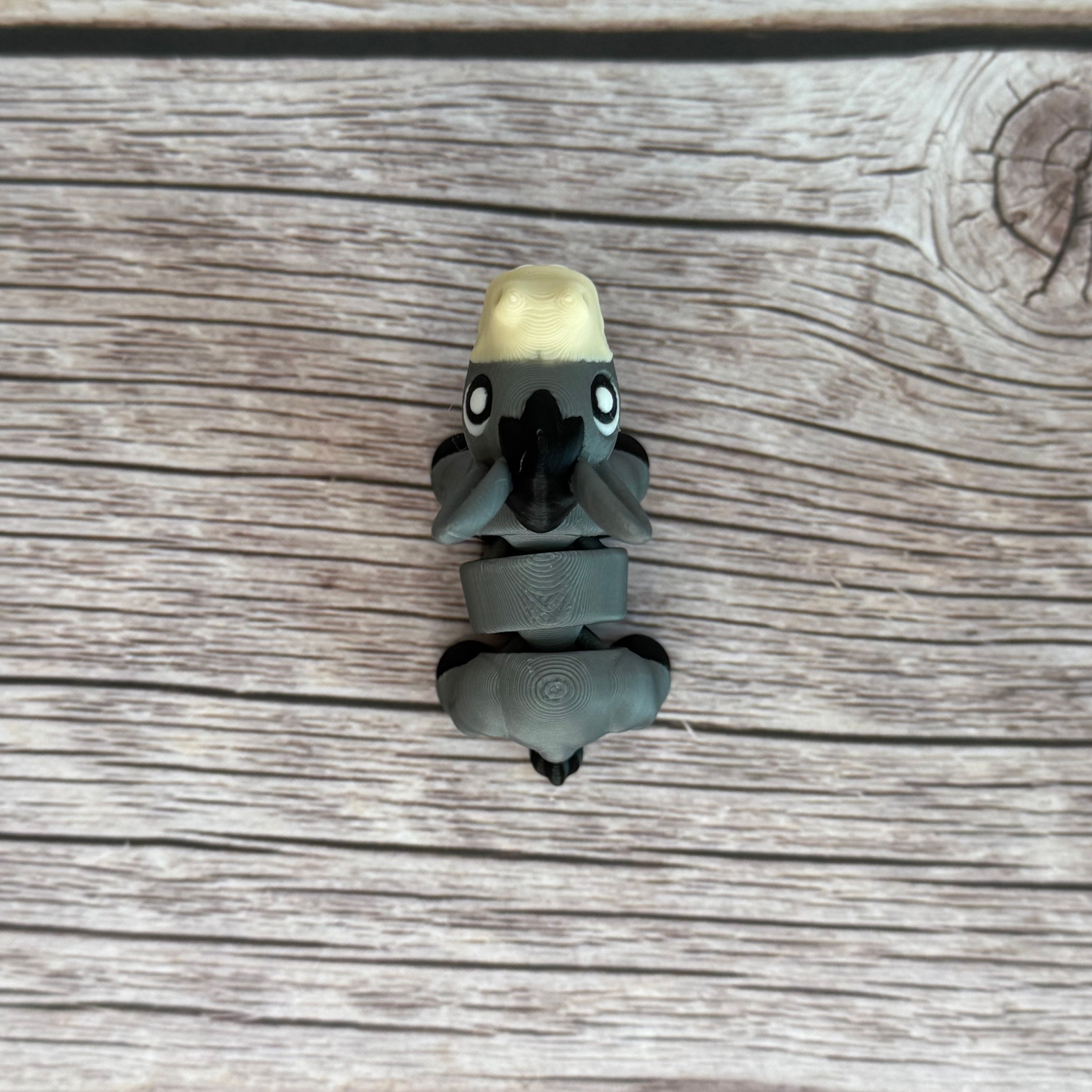 A small 3D printed gray donkey toy with movable segments, positioned on a wooden surface.