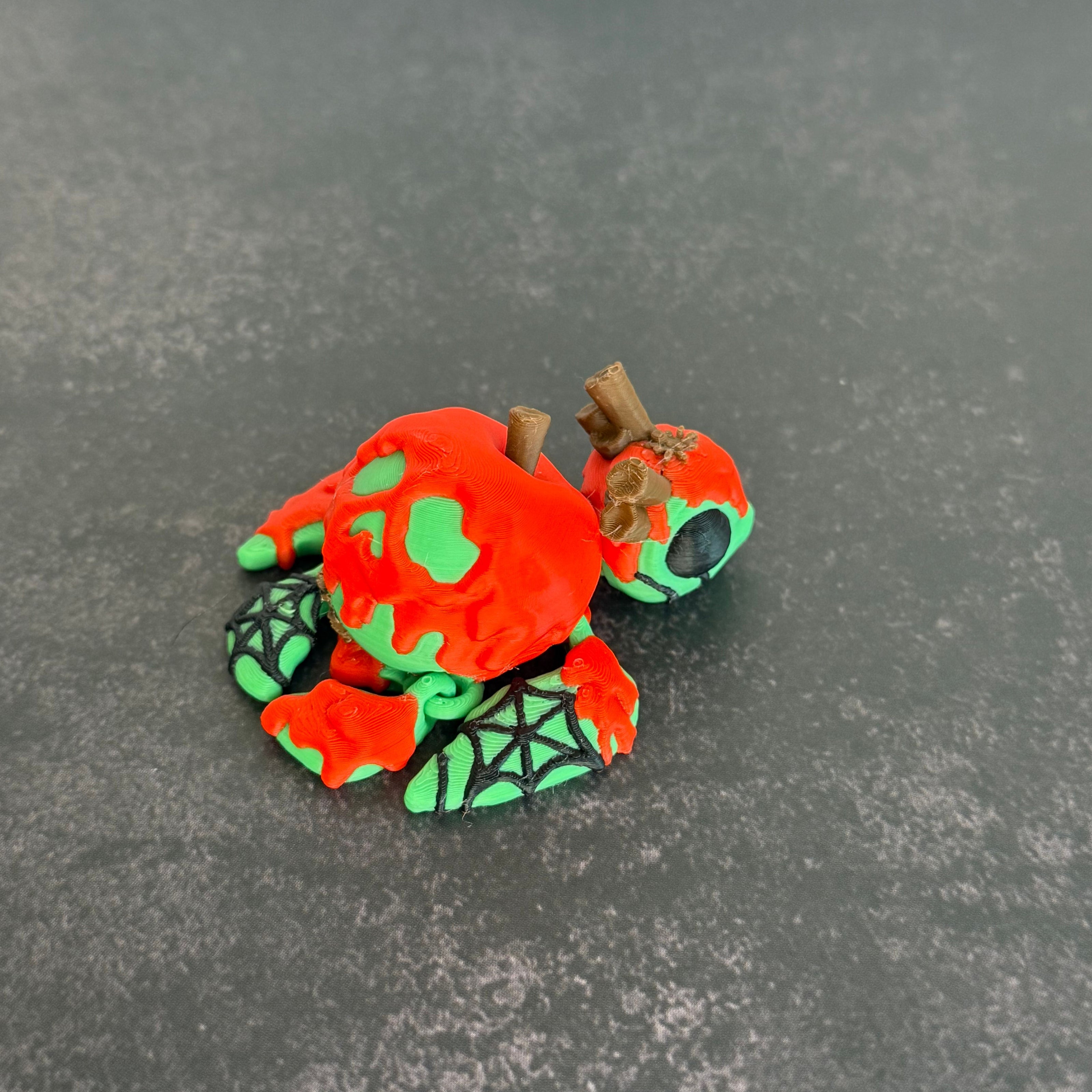 3D printed articulated turtle toy with a toxic apple-inspired shell in red and green, with a black background.