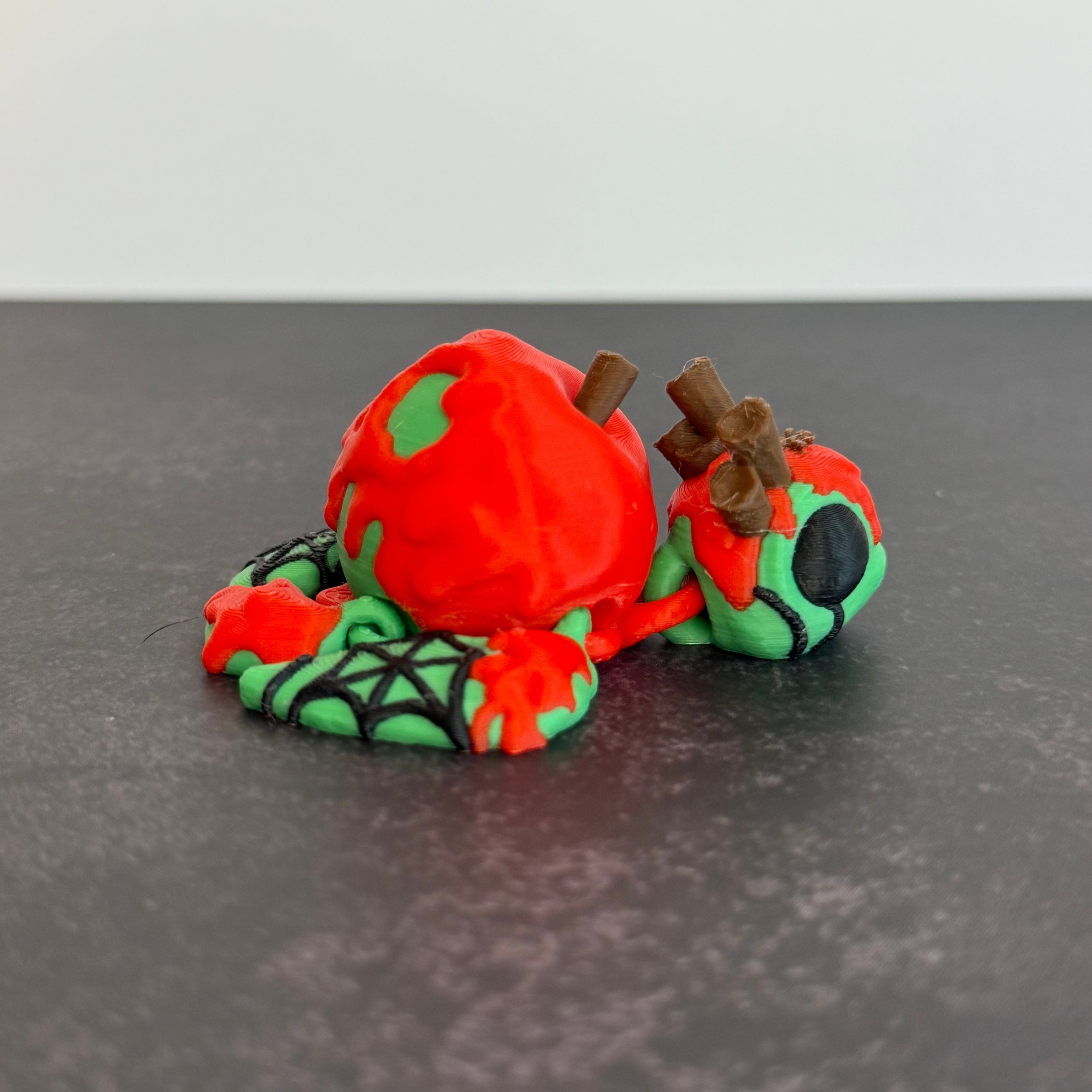 3D printed articulated turtle toy with a toxic apple-inspired shell in red and green, with a black background.