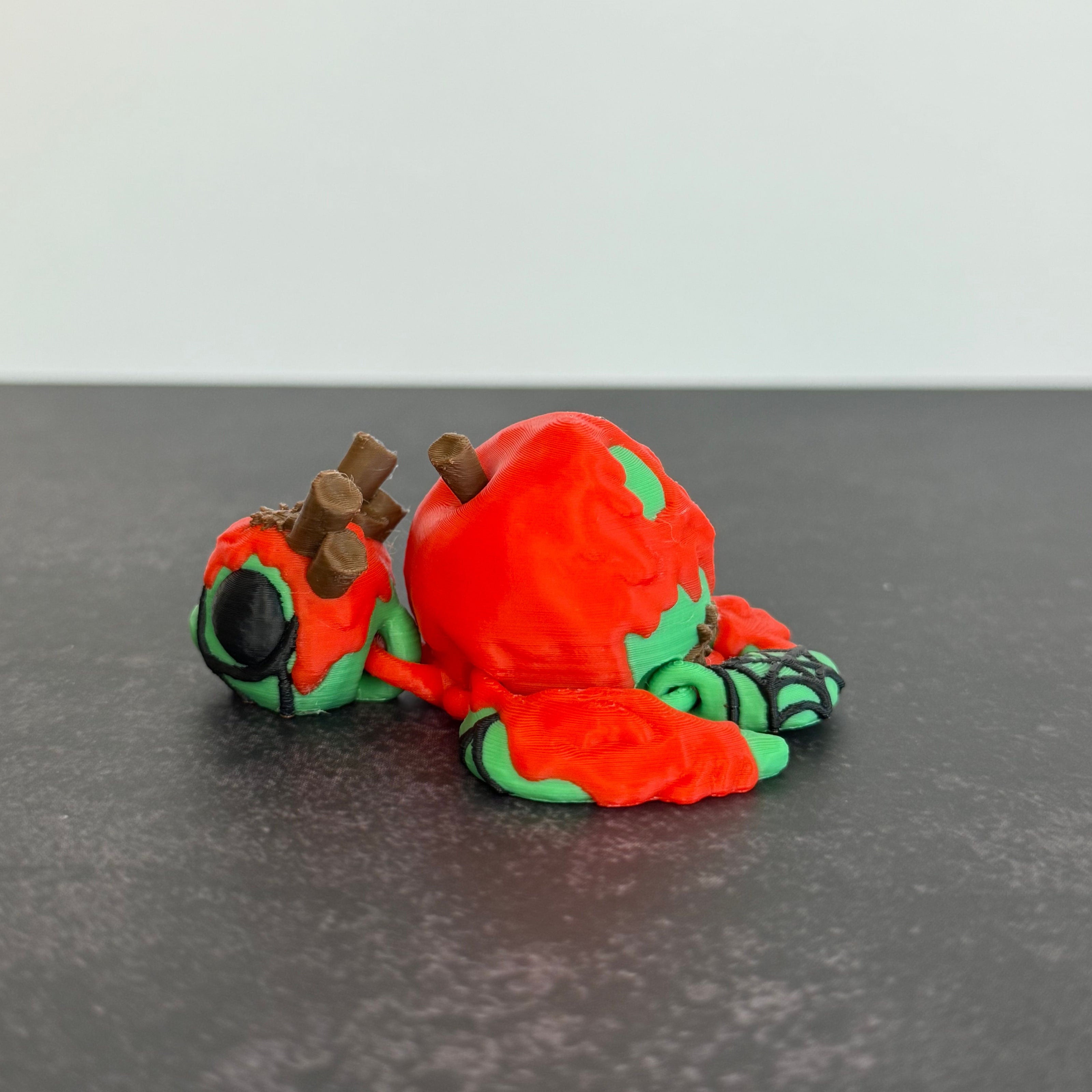 3D printed articulated turtle toy with a toxic apple-inspired shell in red and green, with a black background.