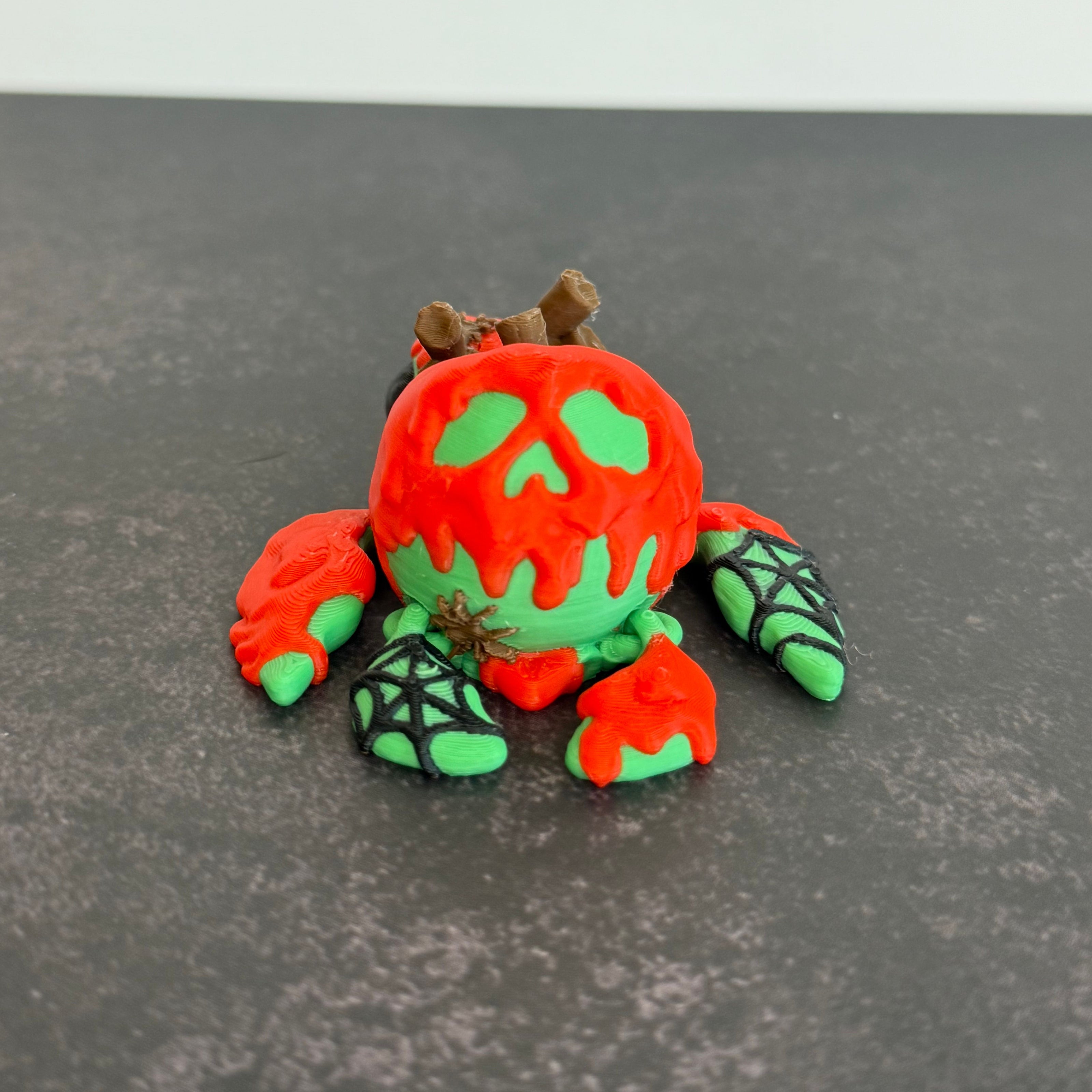 3D printed articulated turtle toy with a toxic apple-inspired shell in red and green, with a black background.