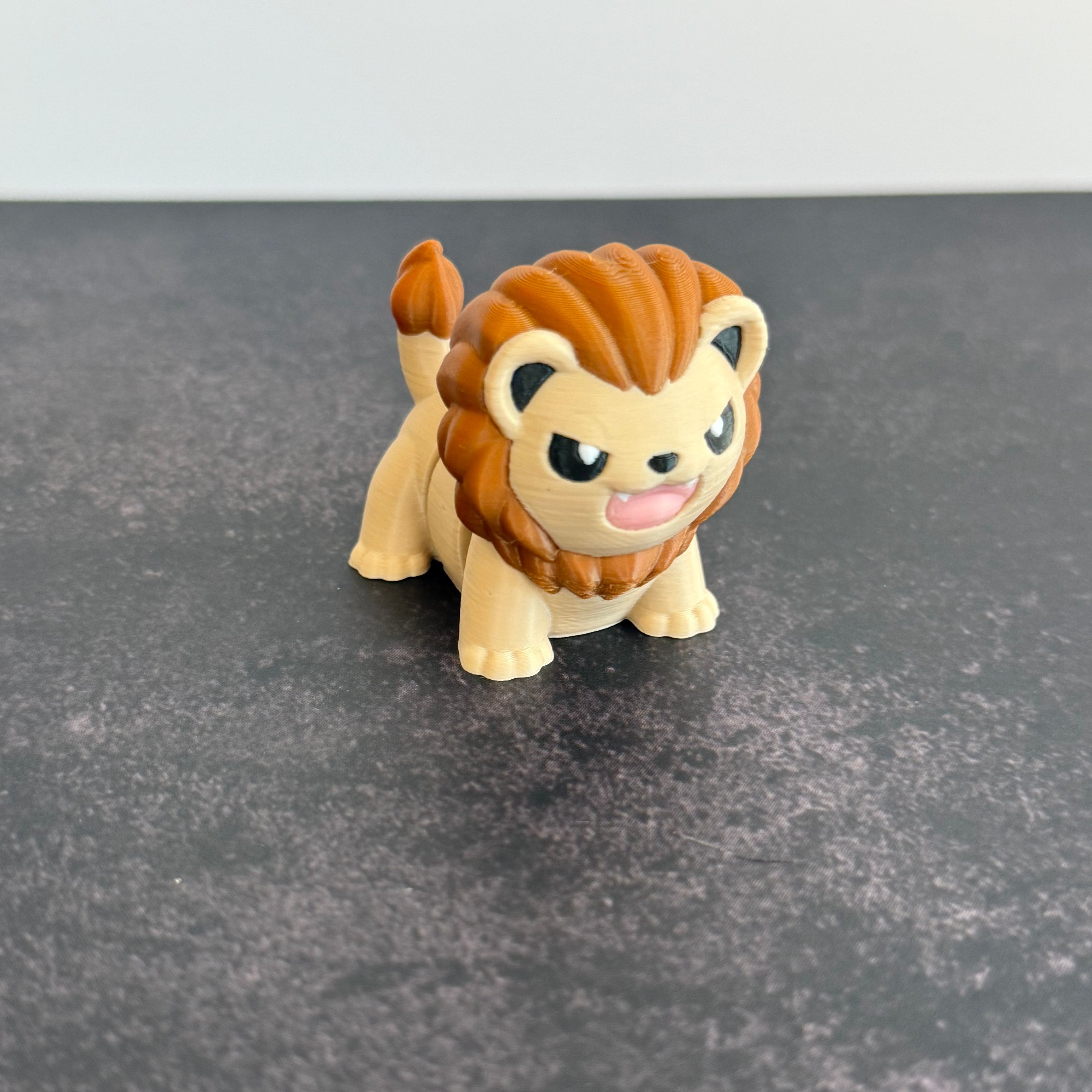 A 3D printed mini articulated lion fidget toy with articulated body segments, placed on a dark surface.