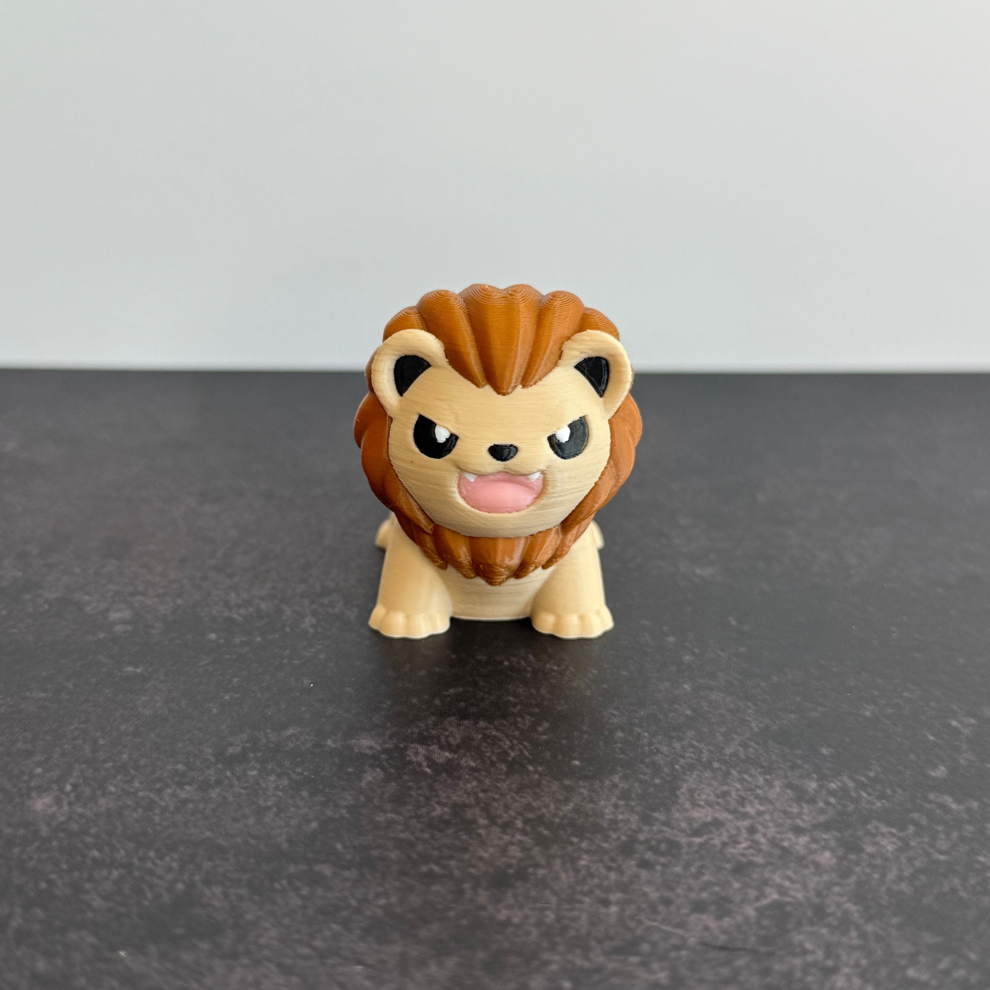 A 3D printed mini articulated lion fidget toy with articulated body segments, placed on a dark surface.