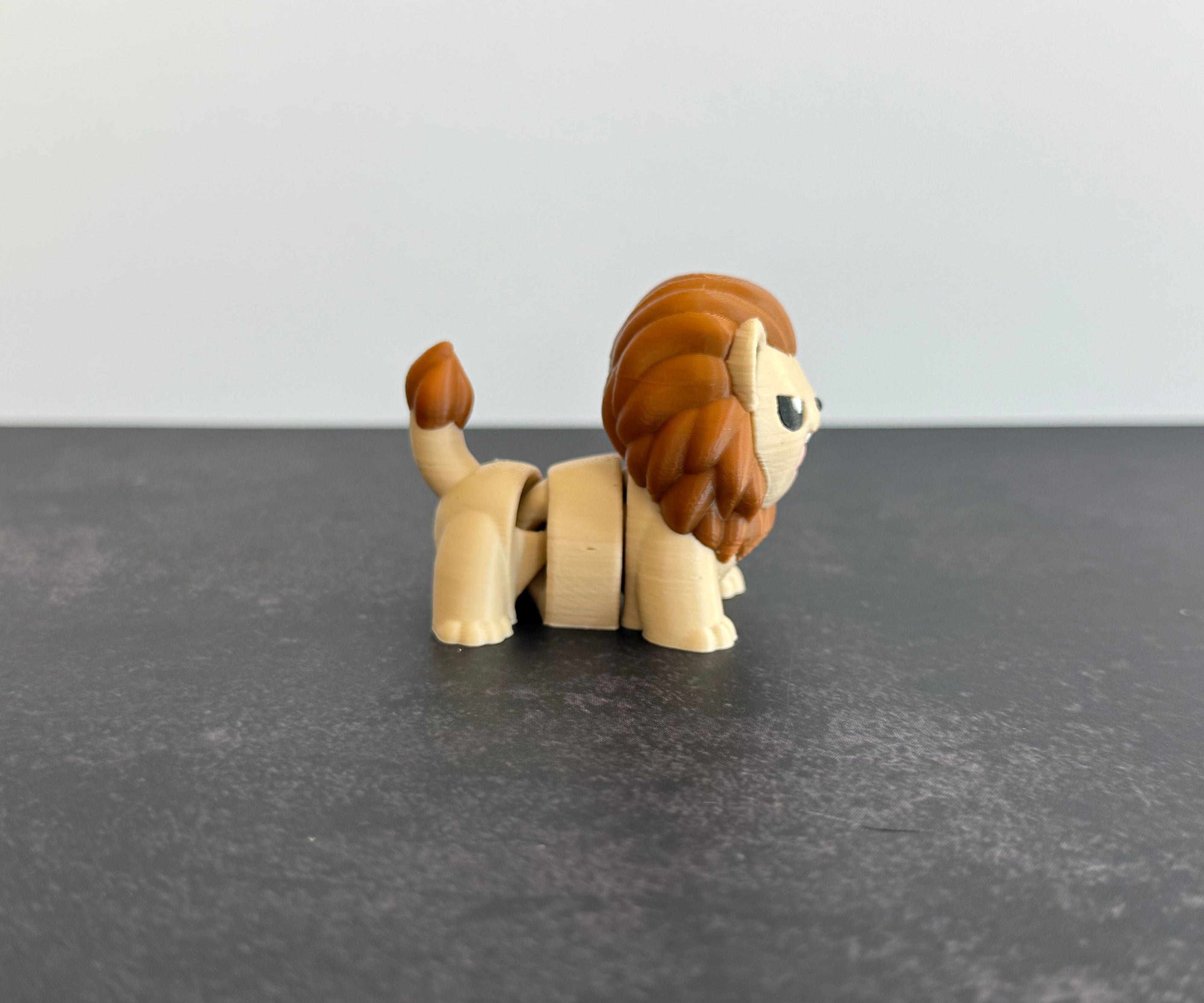 A 3D printed mini articulated lion fidget toy with articulated body segments, placed on a dark surface.