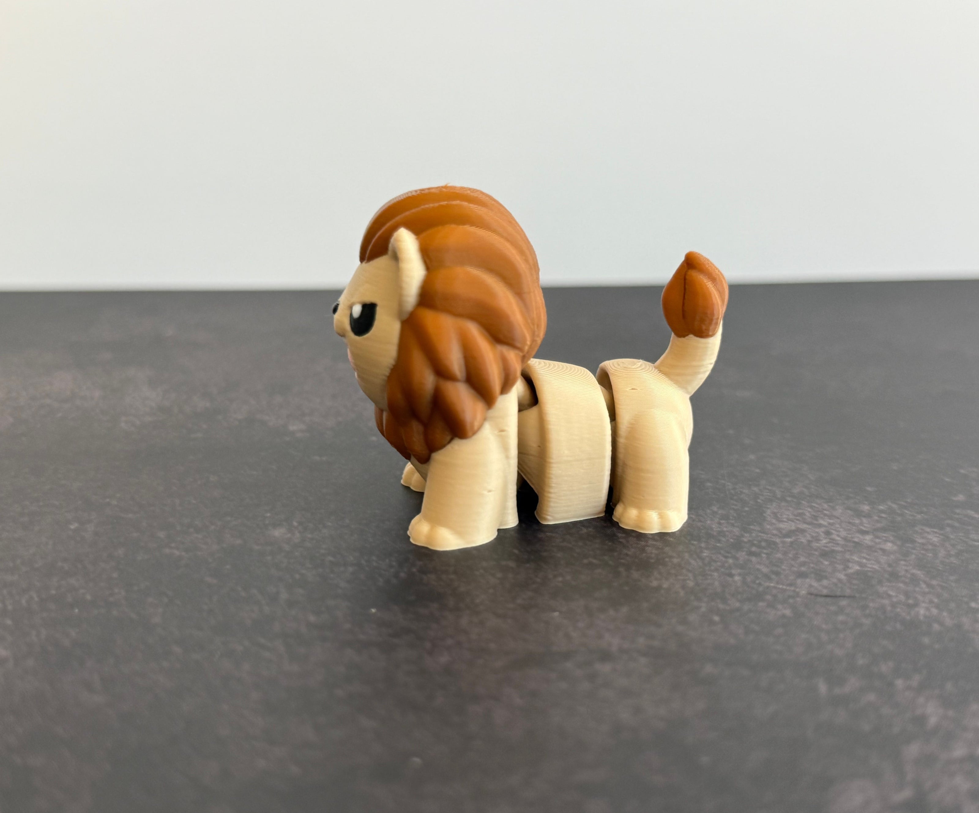 A 3D printed mini articulated lion fidget toy with articulated body segments, placed on a dark surface.