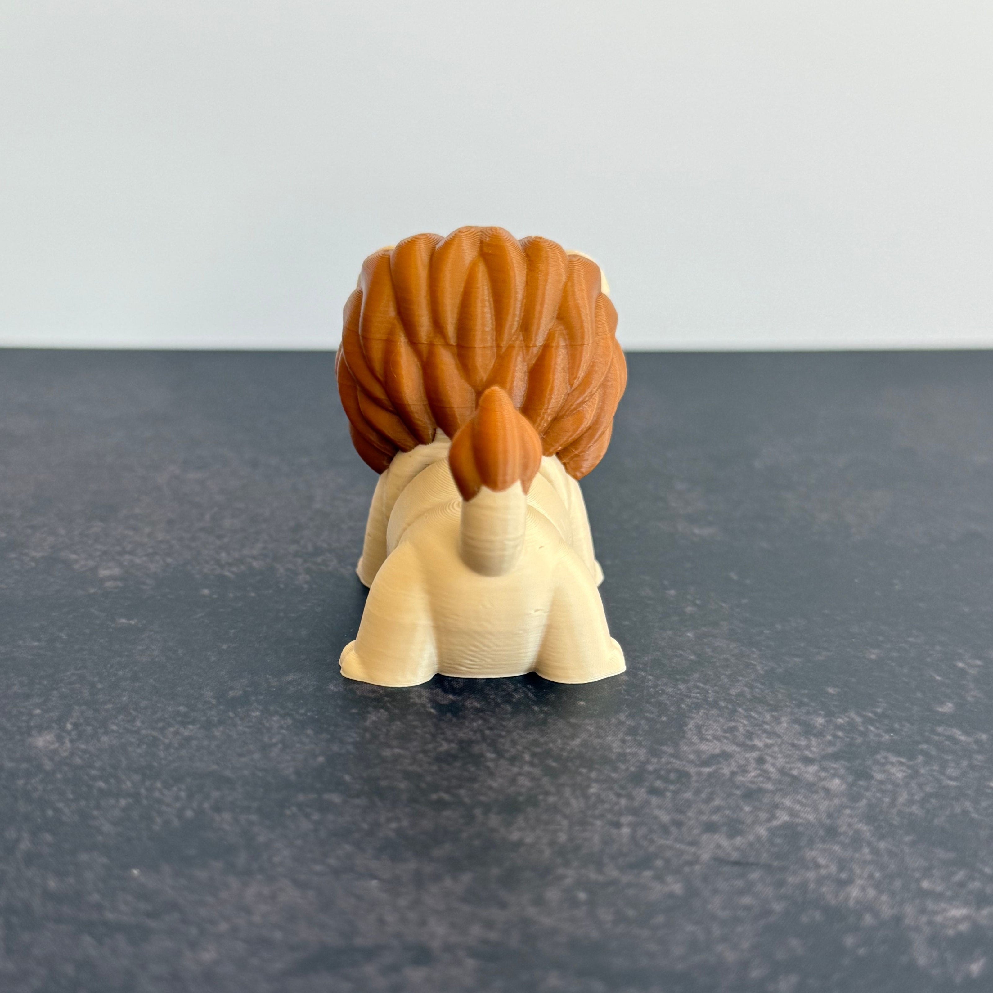 A 3D printed mini articulated lion fidget toy with articulated body segments, placed on a dark surface.