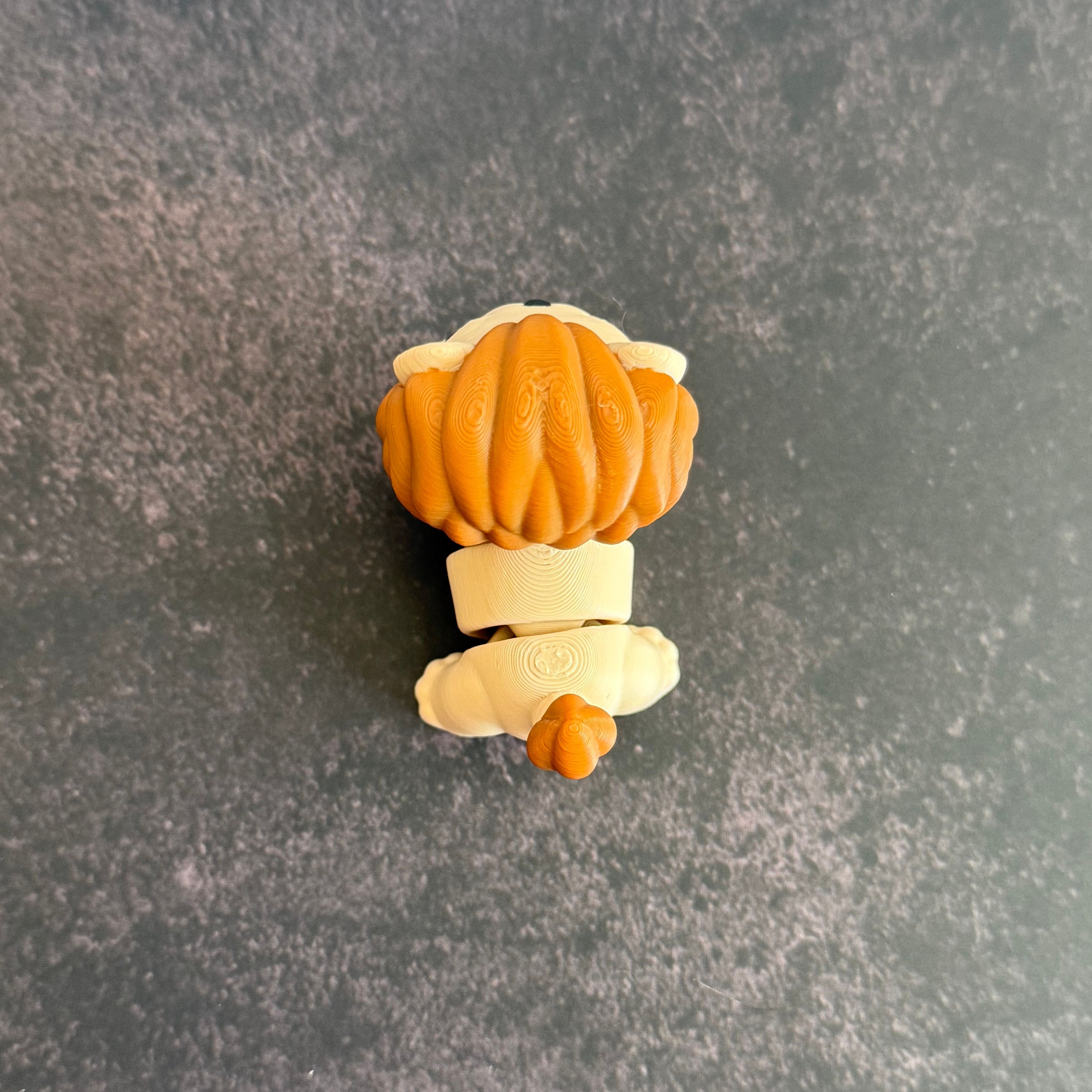 A 3D printed mini articulated lion fidget toy with articulated body segments, placed on a dark surface.