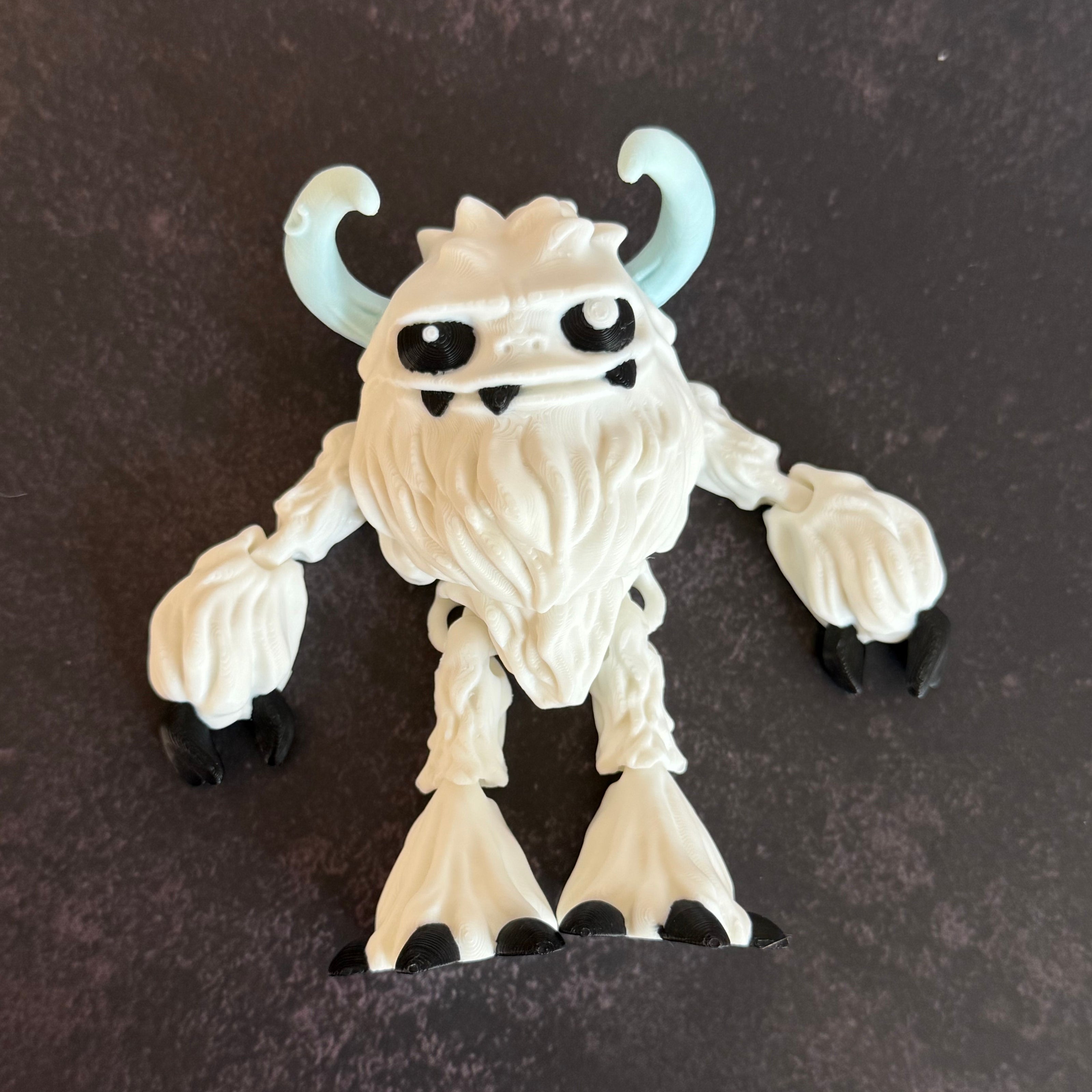 3d-printed toy figure of a yeti creature with white hairy body, black eyes, and blue horns on a gray background
