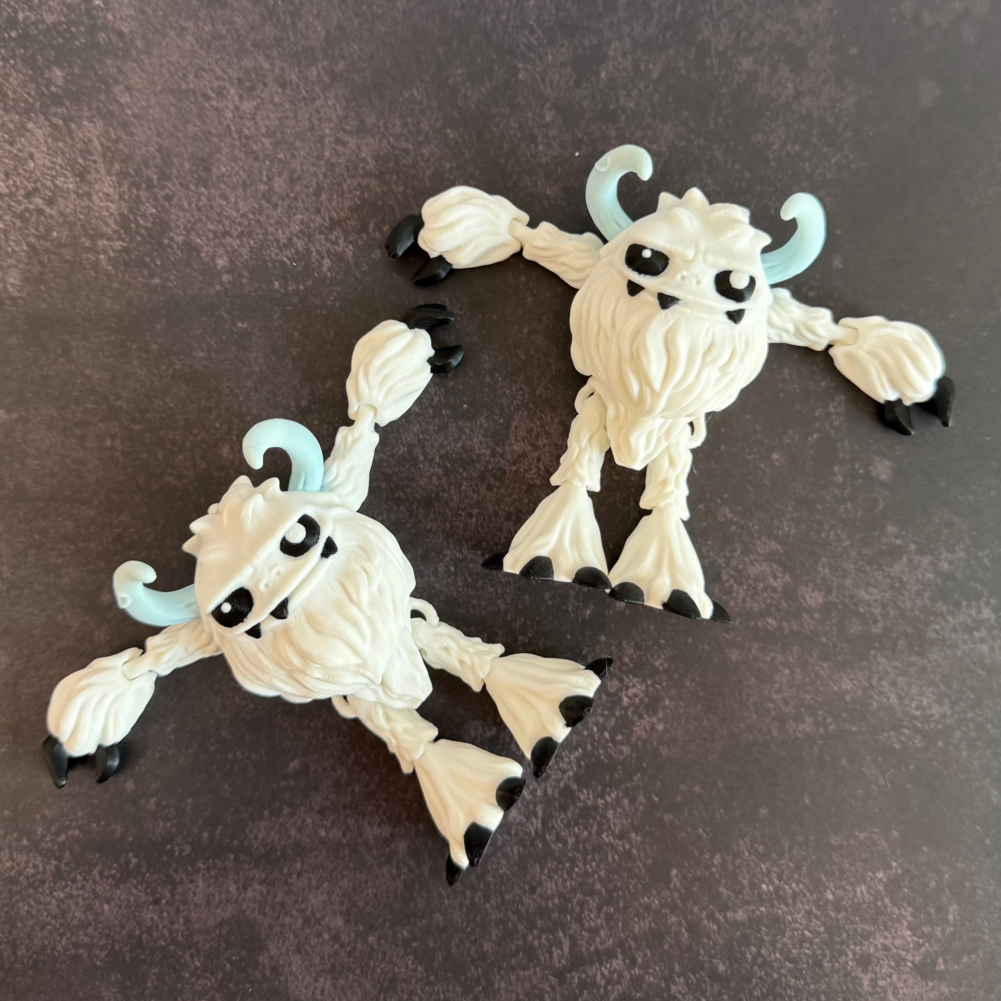 Two white monster-like figurines with black and blue accents on a dark surface