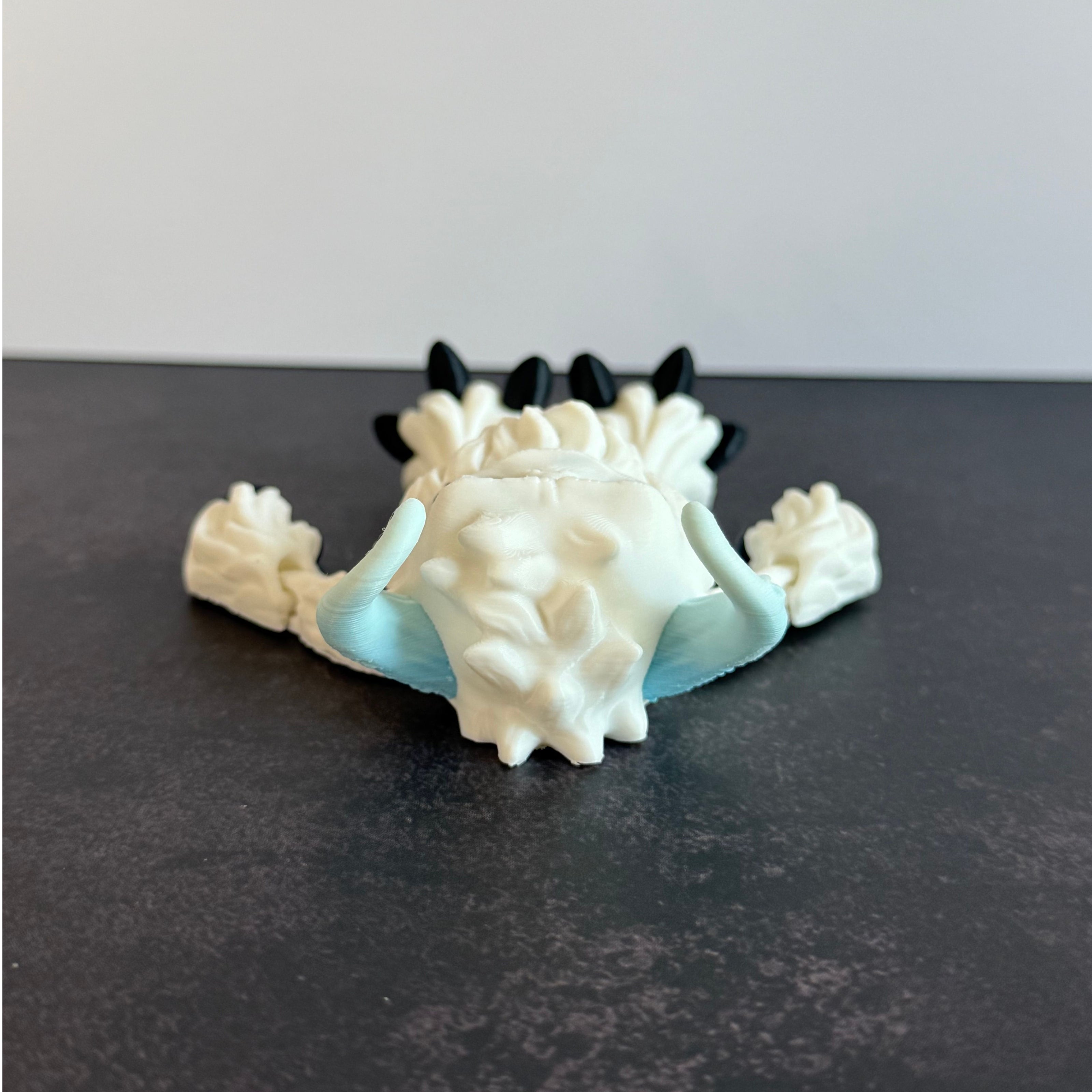 3d-printed toy figure of a yeti creature with white hairy body and blue horns on a black and white background