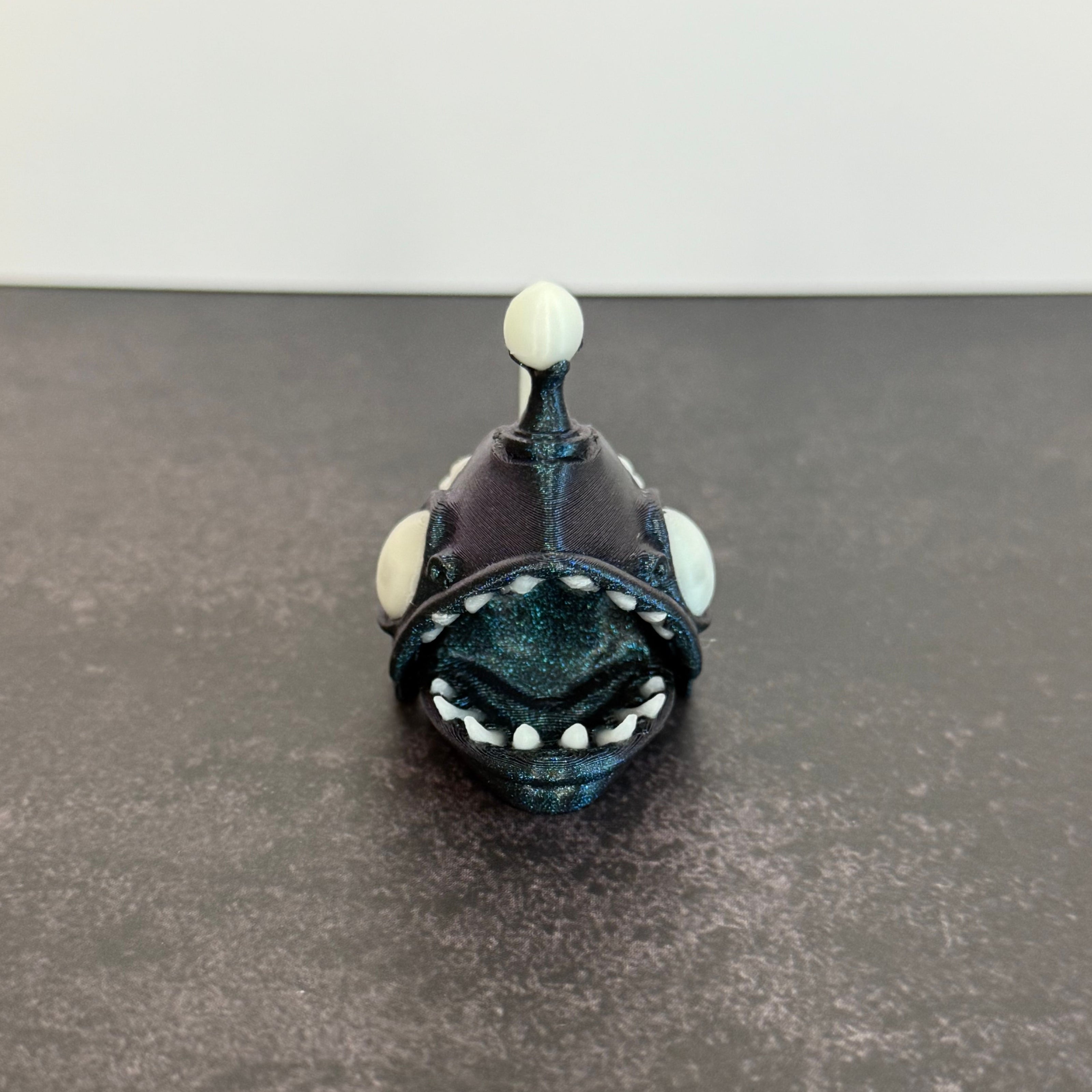Sparkly blue angler fish figurine with white accents on a black and gray background