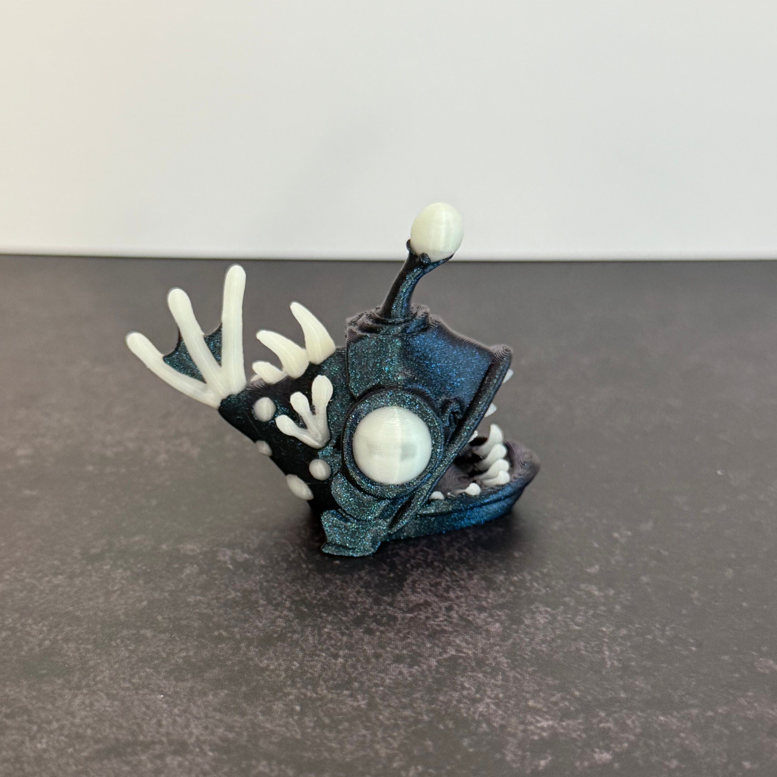 Sparkly blue angler fish figurine with white accents on a black and gray background