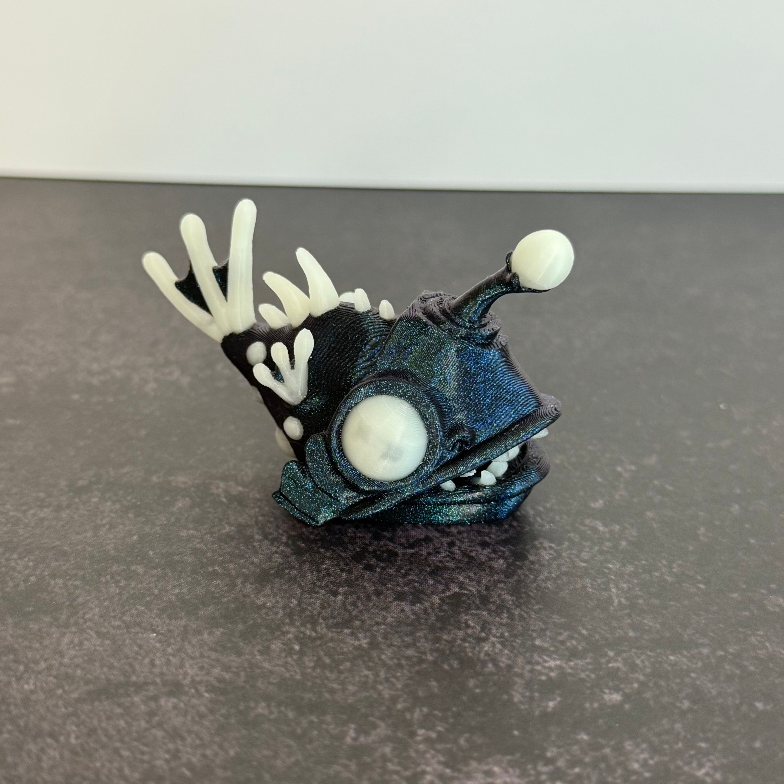 Sparkly blue angler fish figurine with white accents on a black and gray background