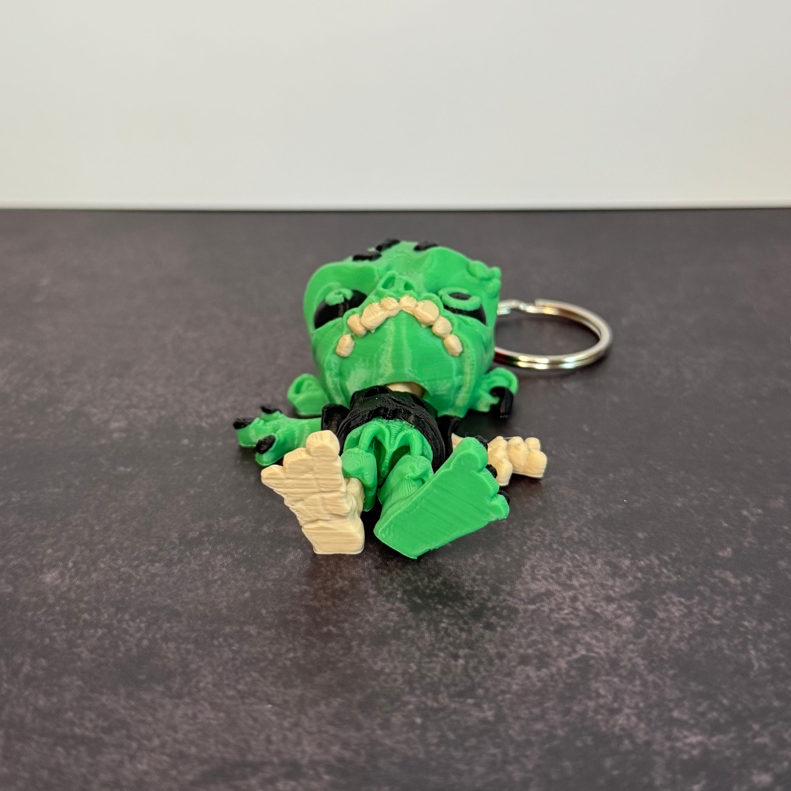 Zombie keychain with green skin, black eyes, and skeleton foot on a black background
