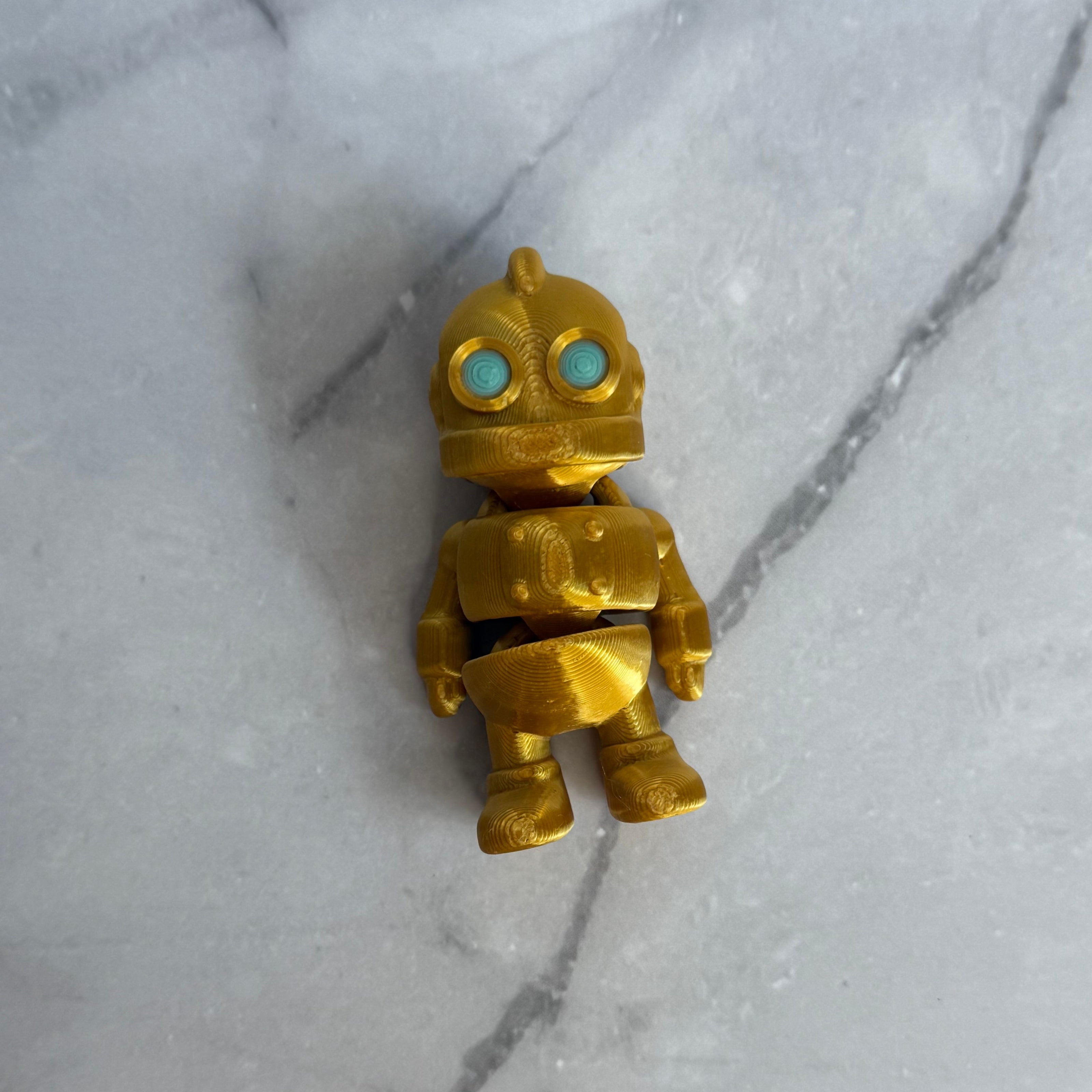 Gold robot figurine with turquoise eyes on a marble background