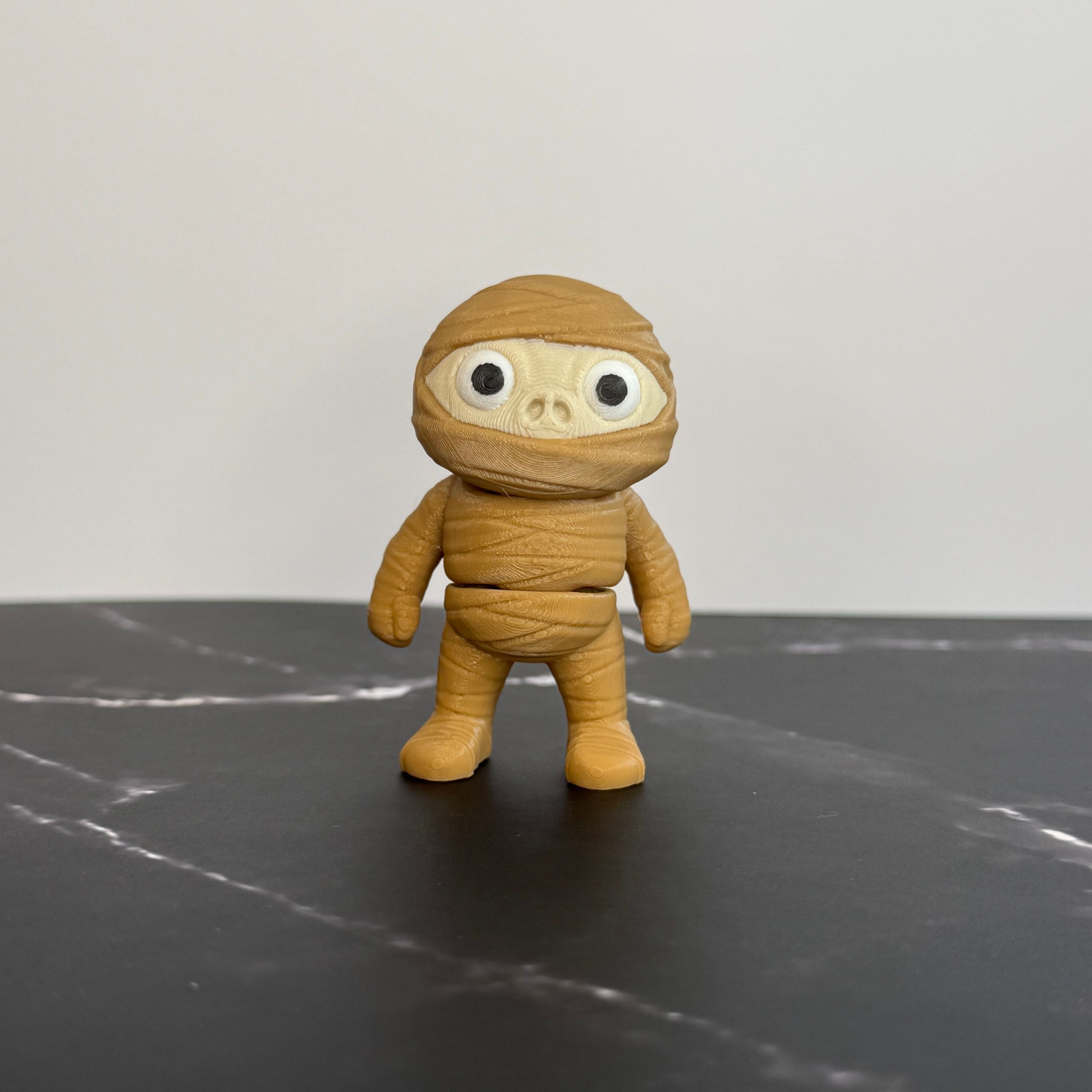 Toy figure of a mummy on a dark surface with a light gray background