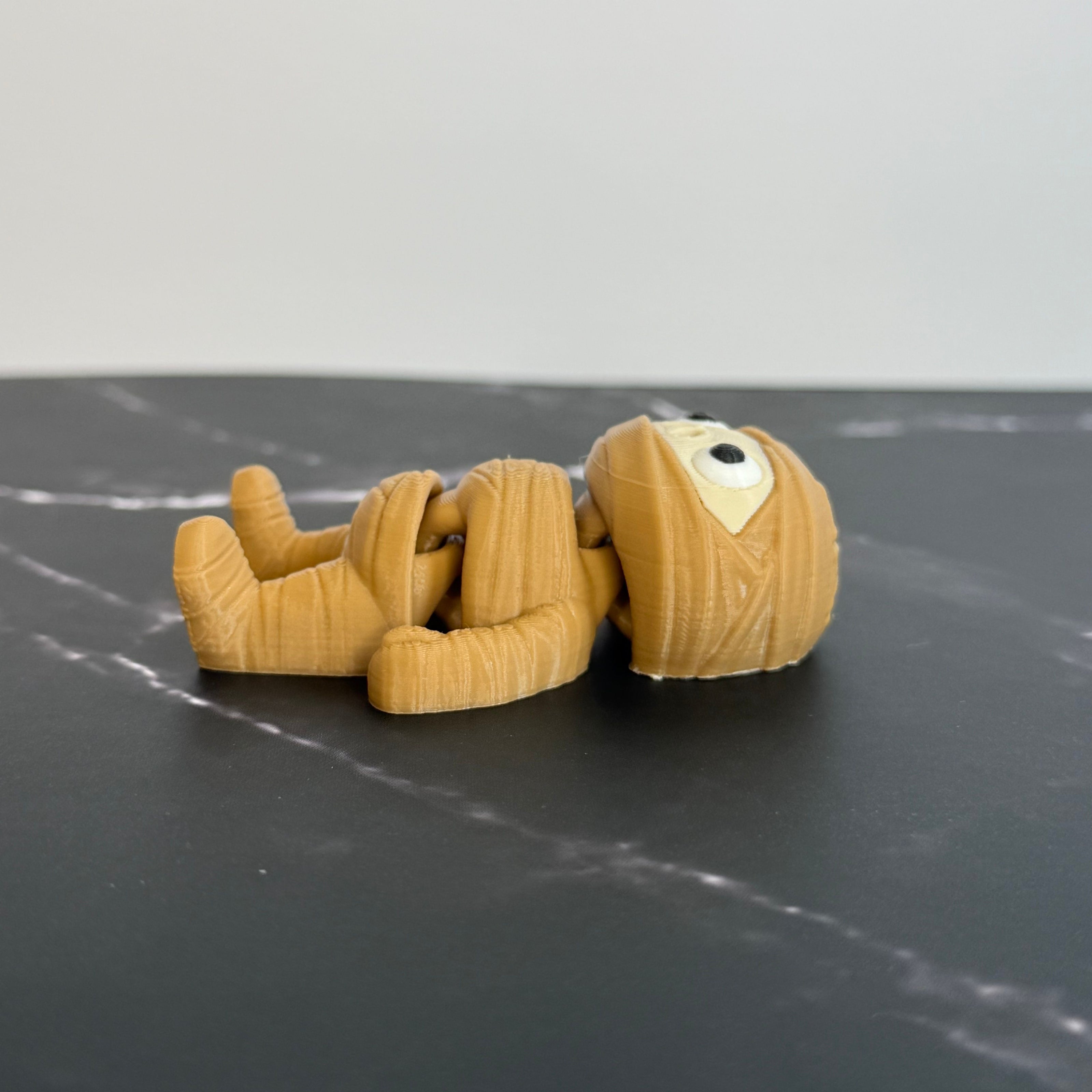 3D-printed mummy toy on a black marble surface