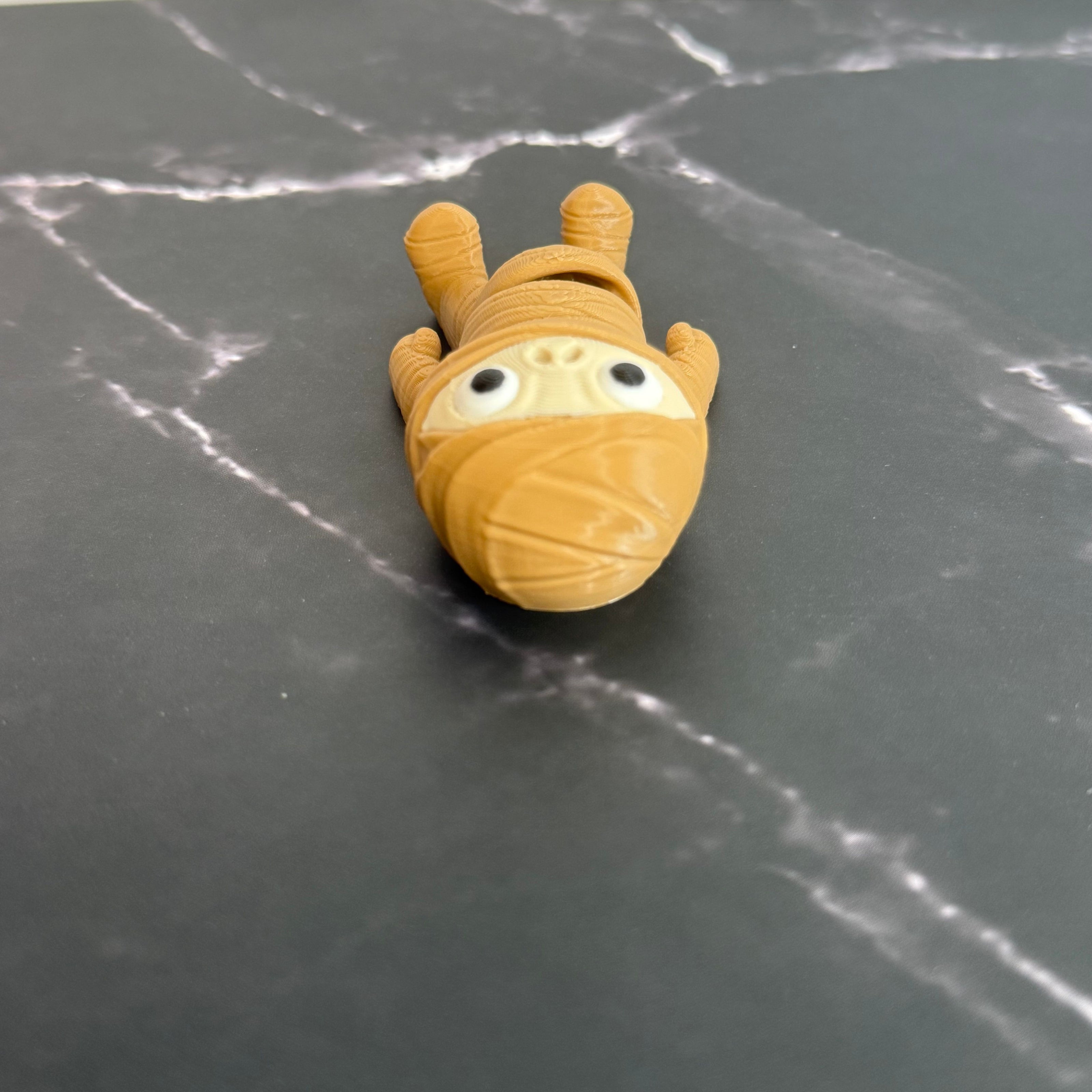 3D-printed mummy toy on a black marble surface