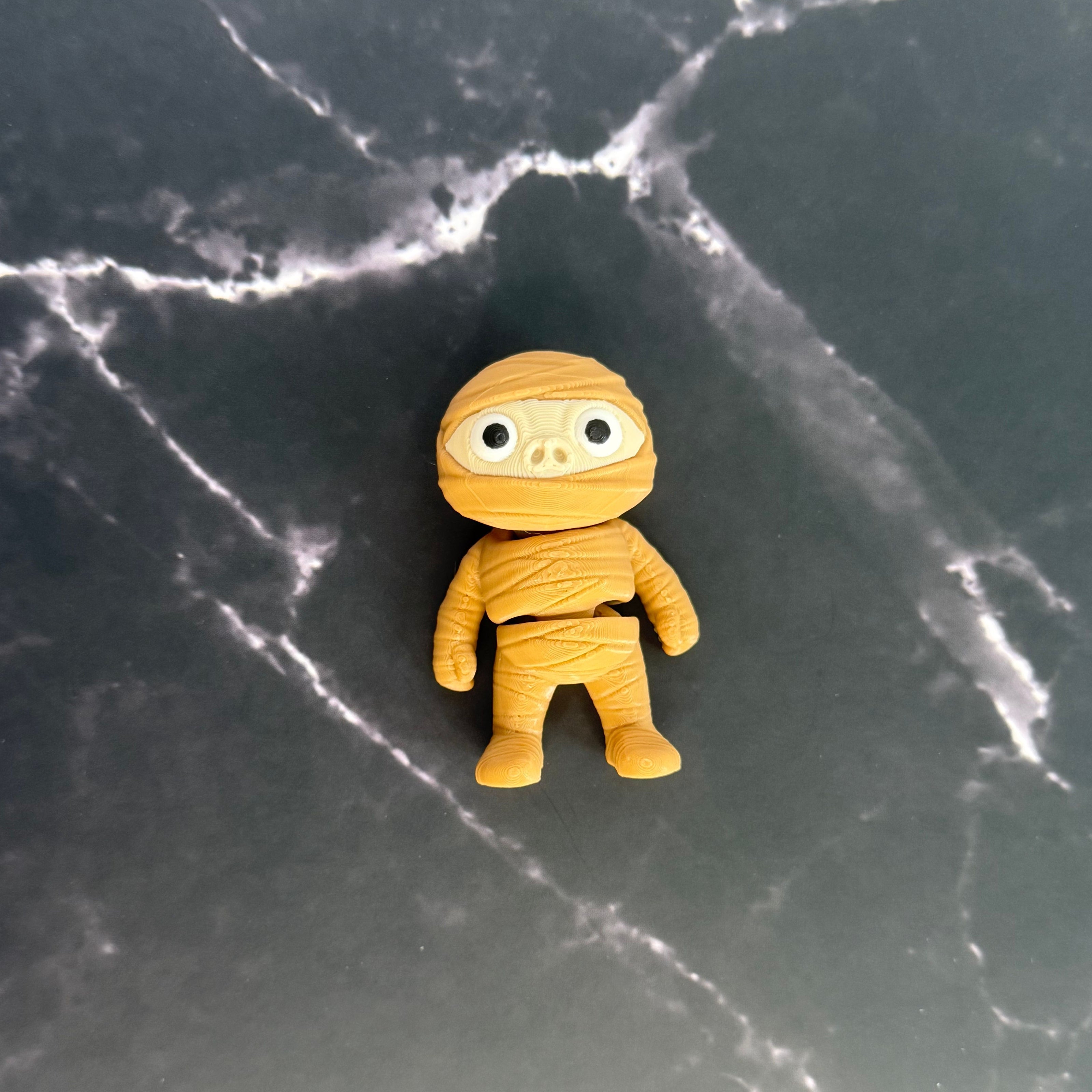 Small yellow mummy figurine on a dark marble surface