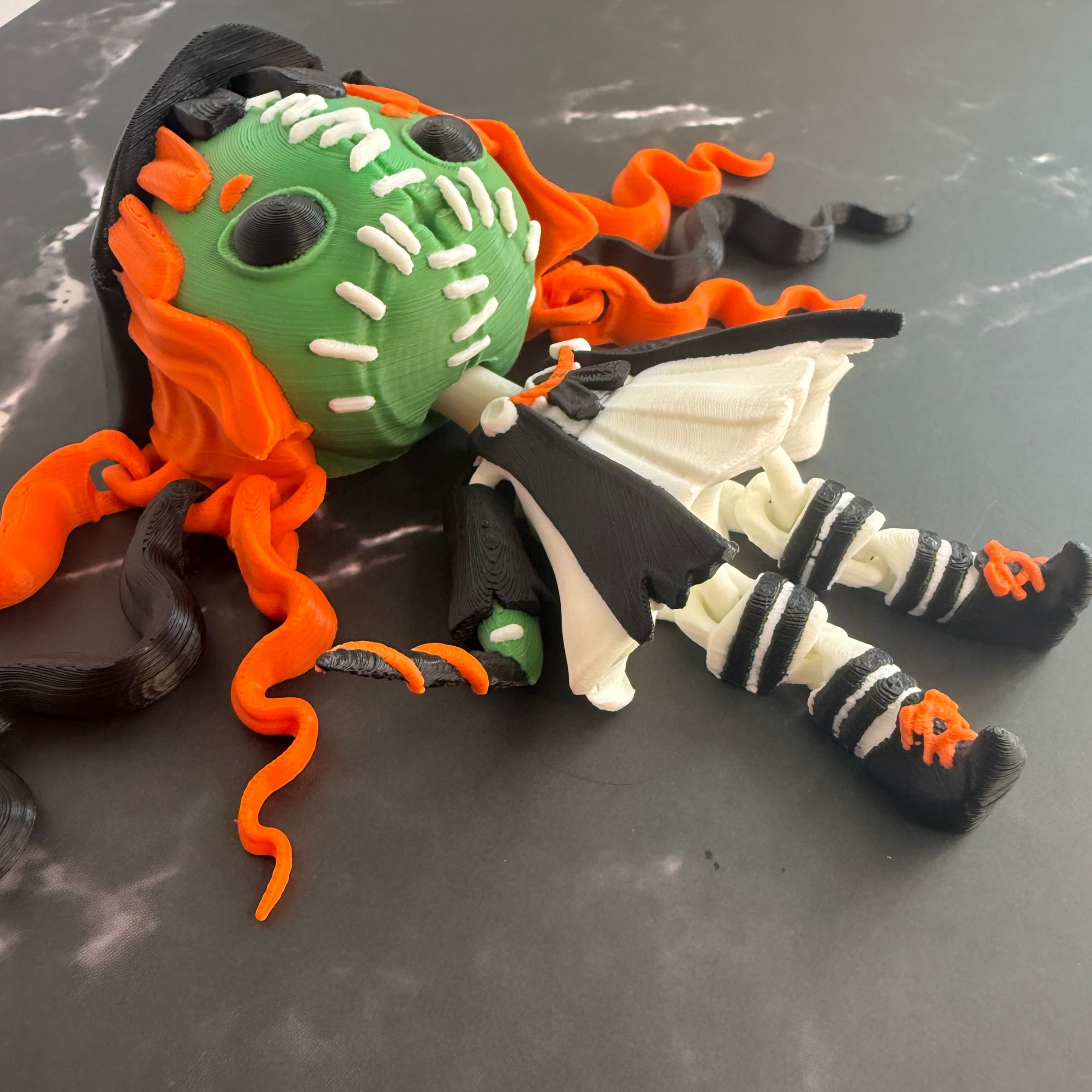 Toy figure with green face, orange hair, and black and white outfit on a gray surface