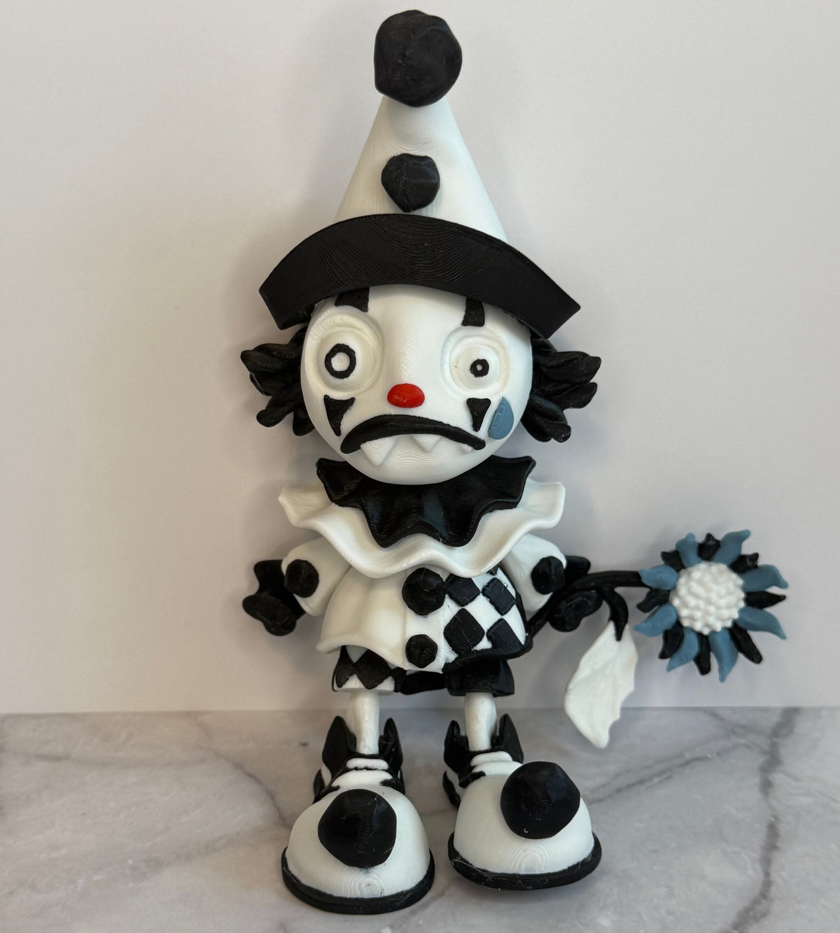 Black and white clown figurine with a hat and checkered outfit on a gray background