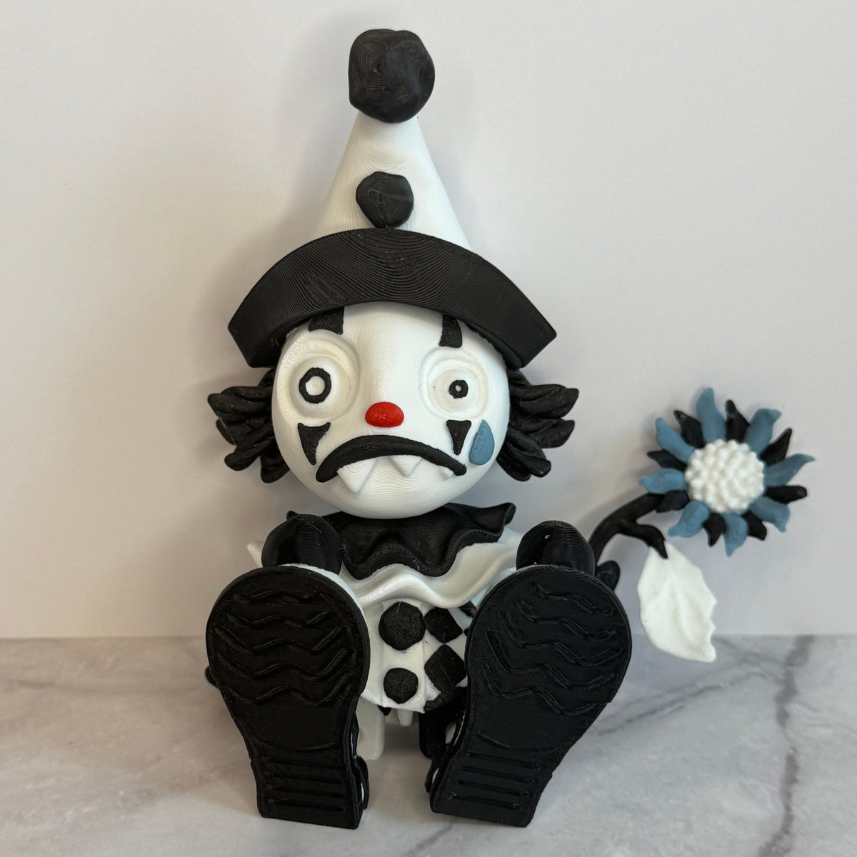 Black and white clown figurine with a hat and checkered outfit on a gray background