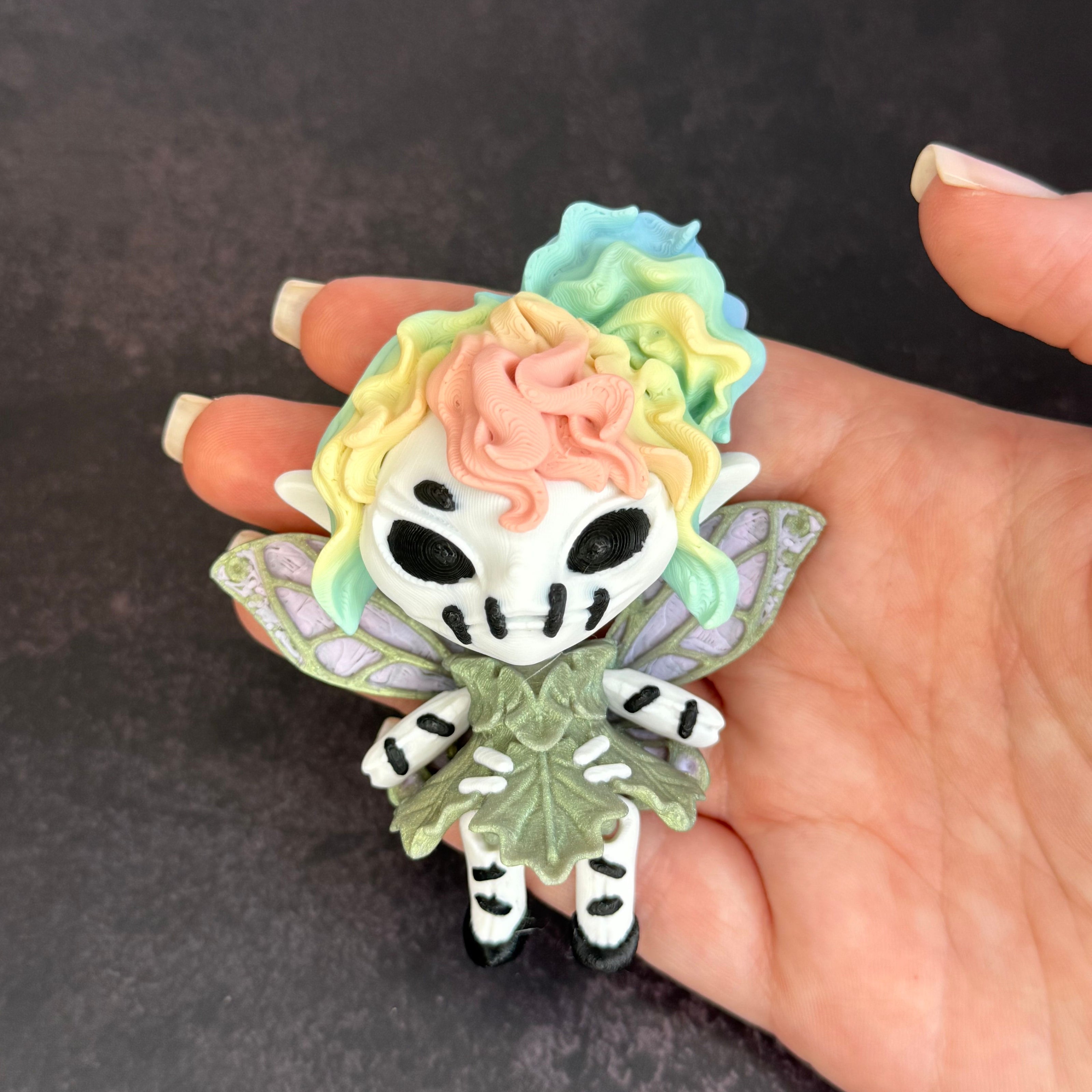 Colorful character with rainbow hair and green dress with green and purple wings on a hand against a black background