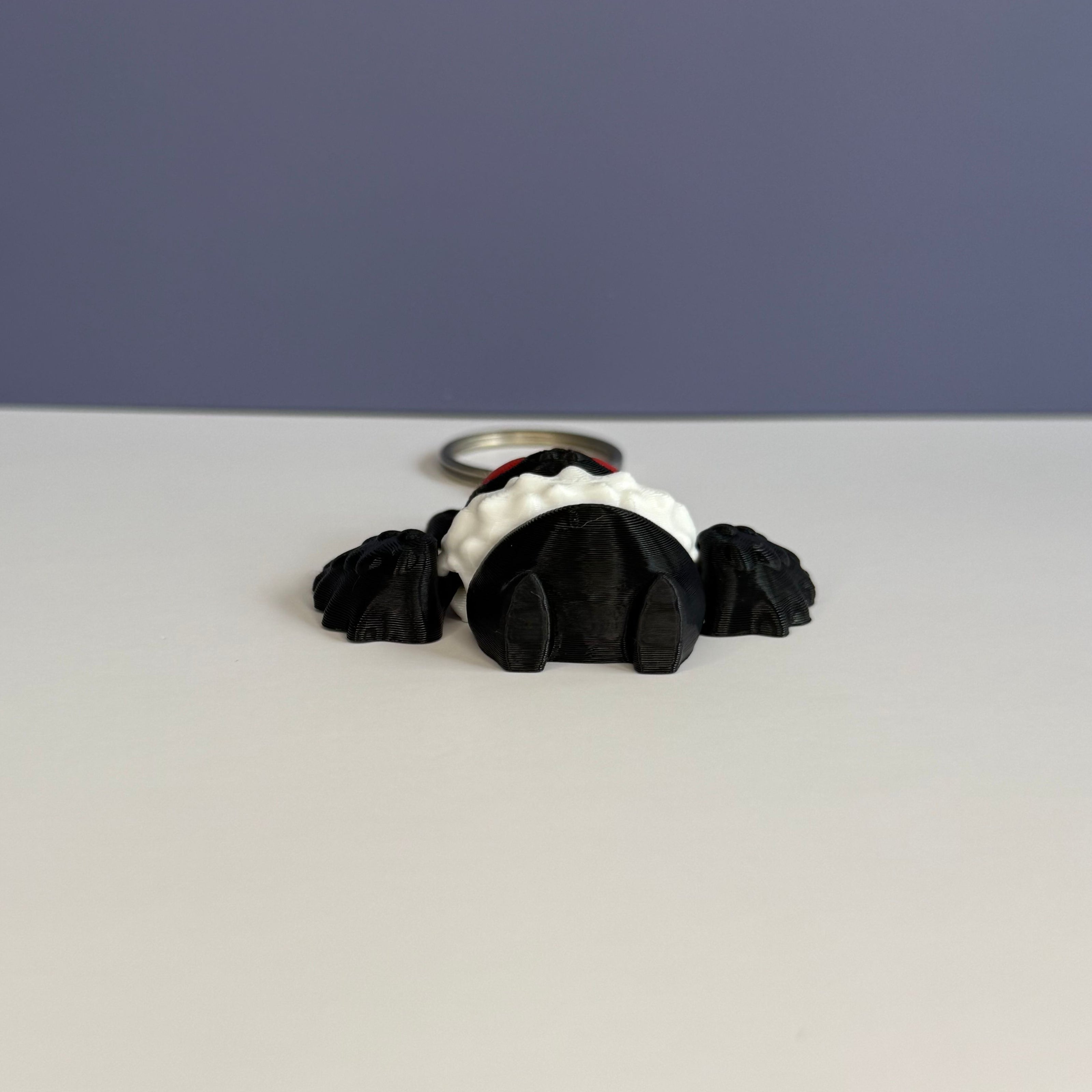 Bottom of a black and white character with wings keychain with red eyes on a blue and white background
