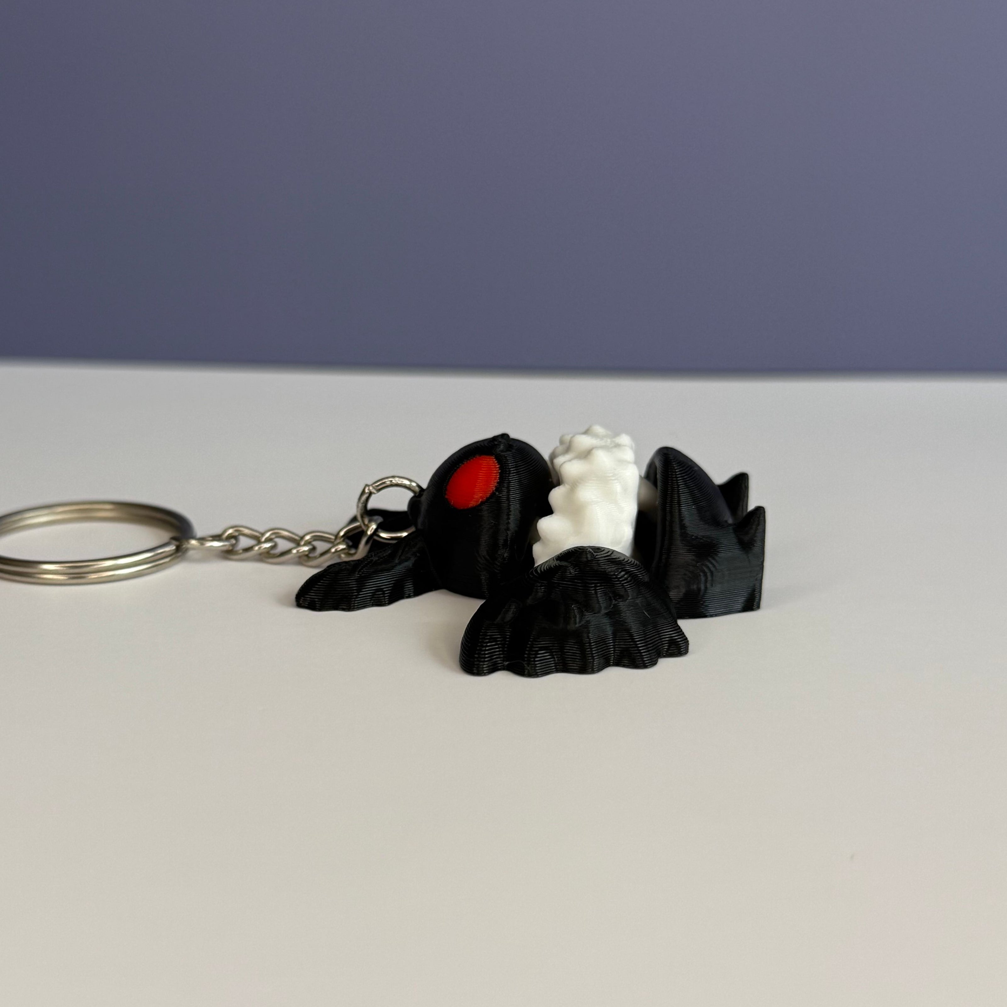 Side of a black and white character with wings keychain with red eyes on a white and blue background