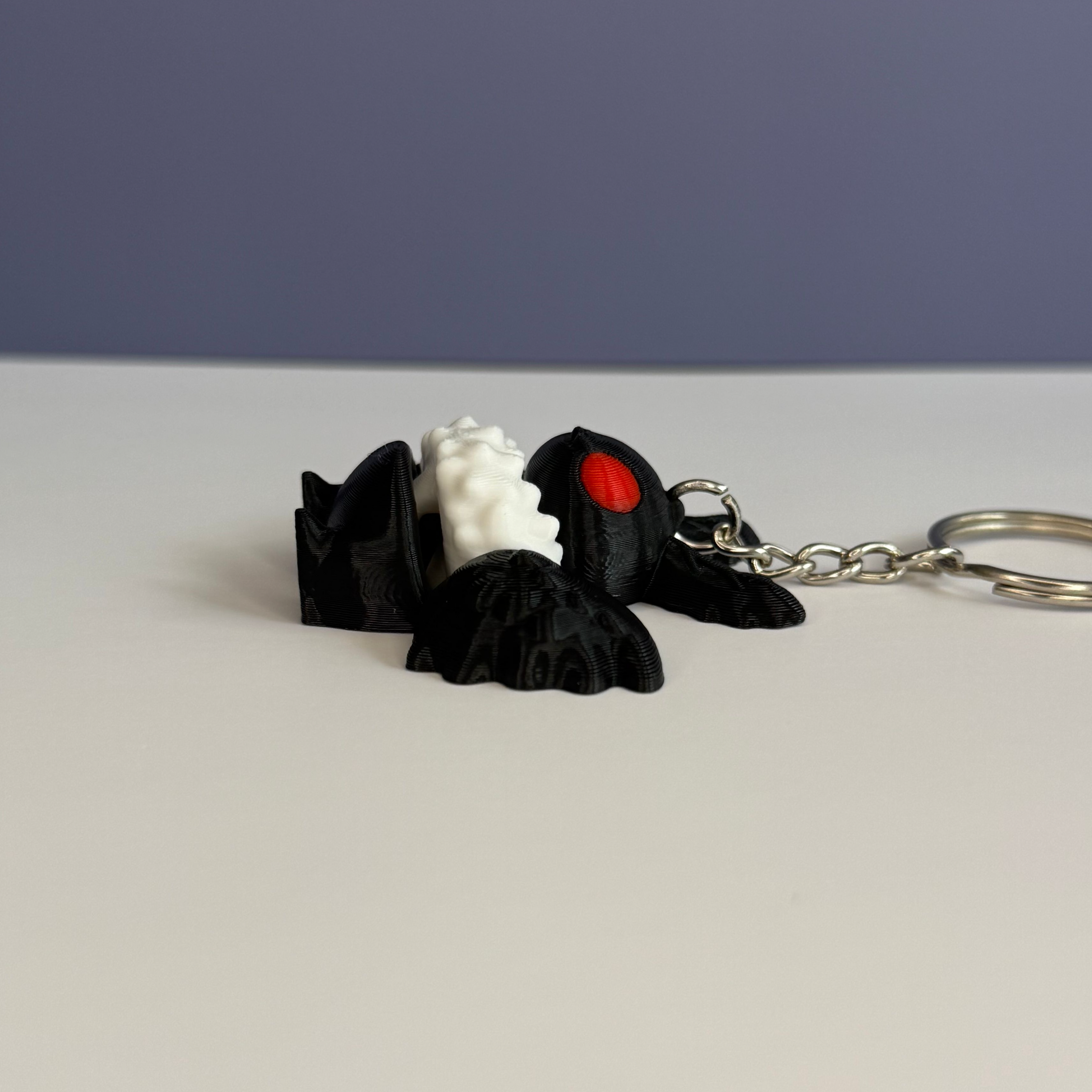 Side of a black and white character with wings keychain with red eyes on a white and blue background