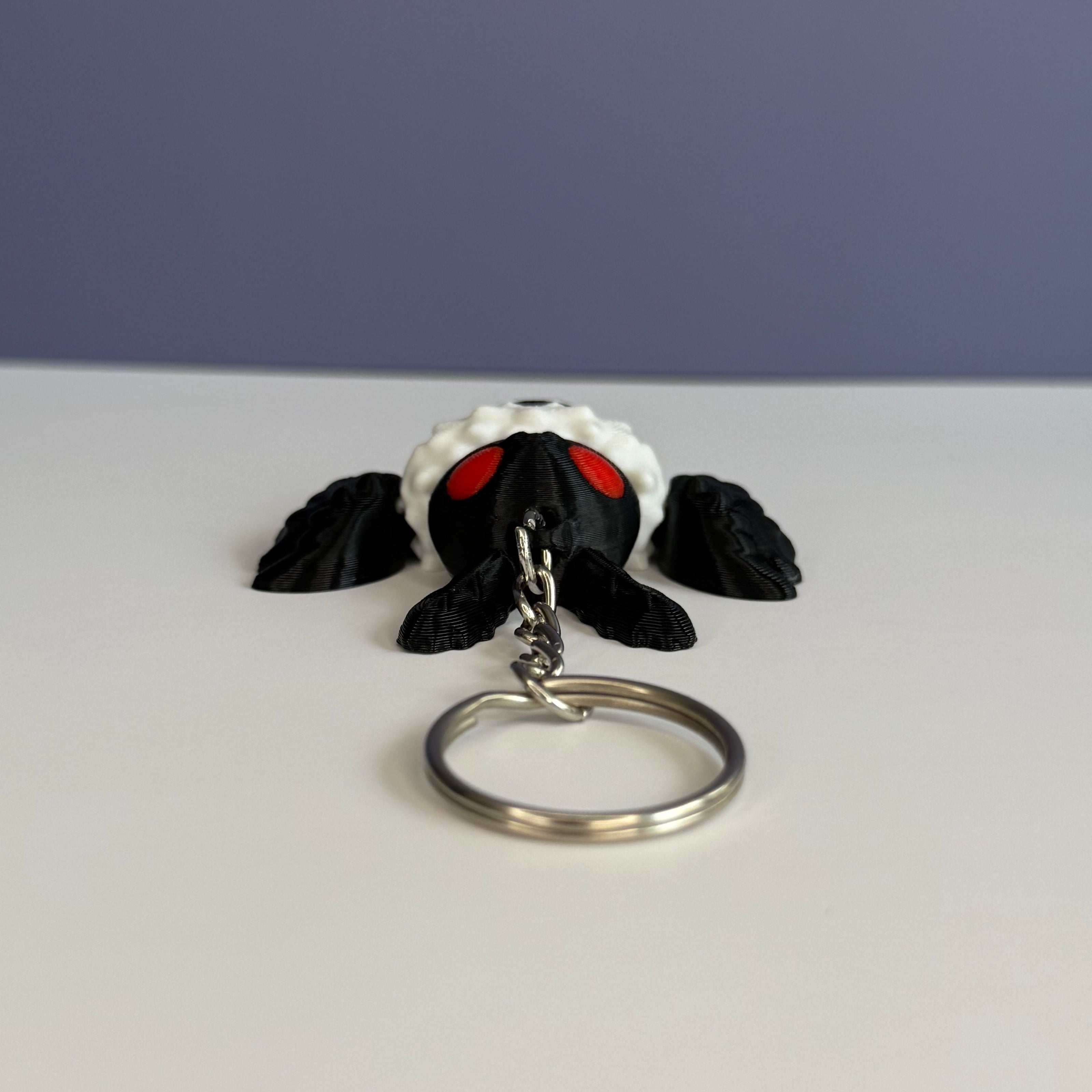 Top of a black and white character with wings keychain with red eyes on a white and blue background