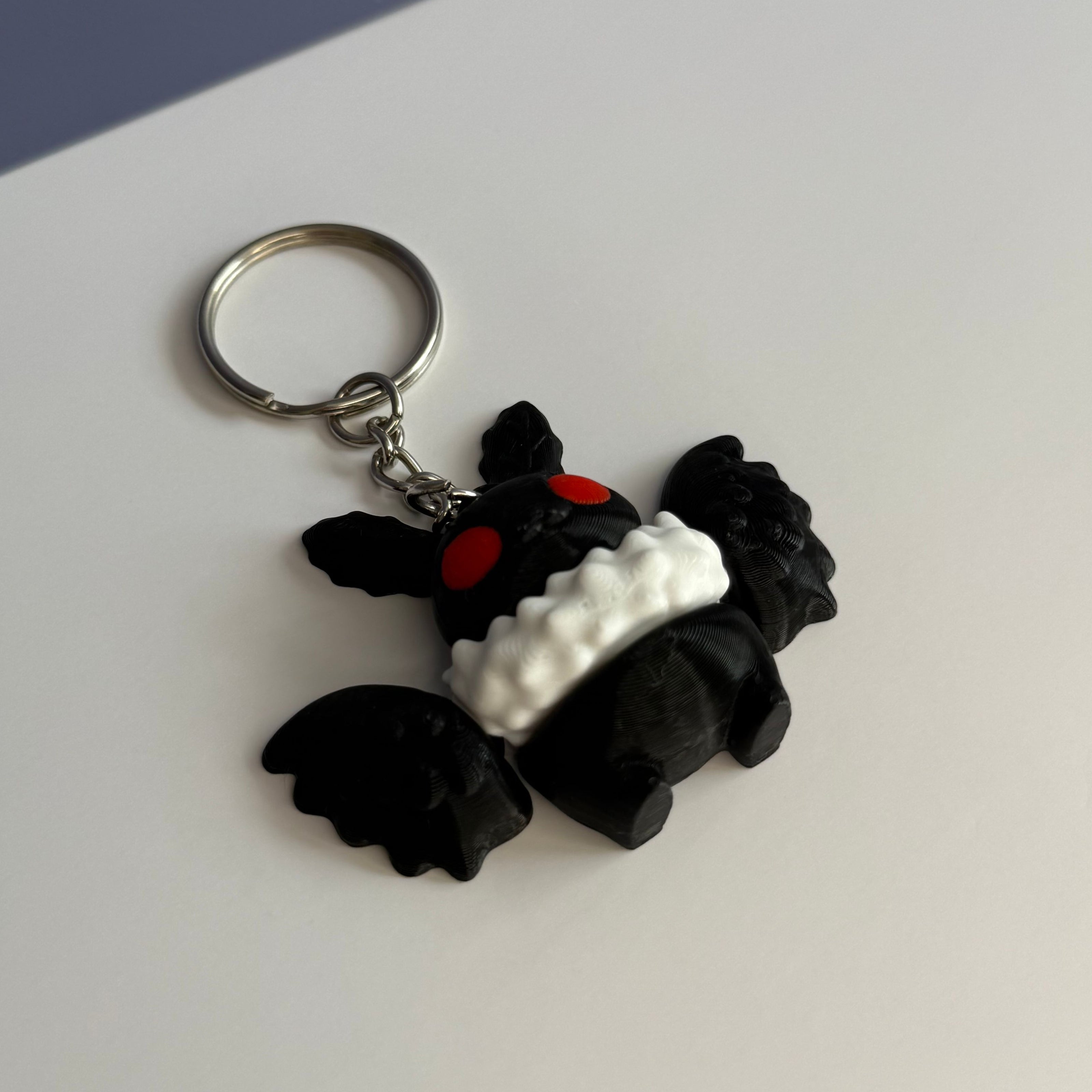 Black and white character with wings keychain with red eyes on a white and blue background