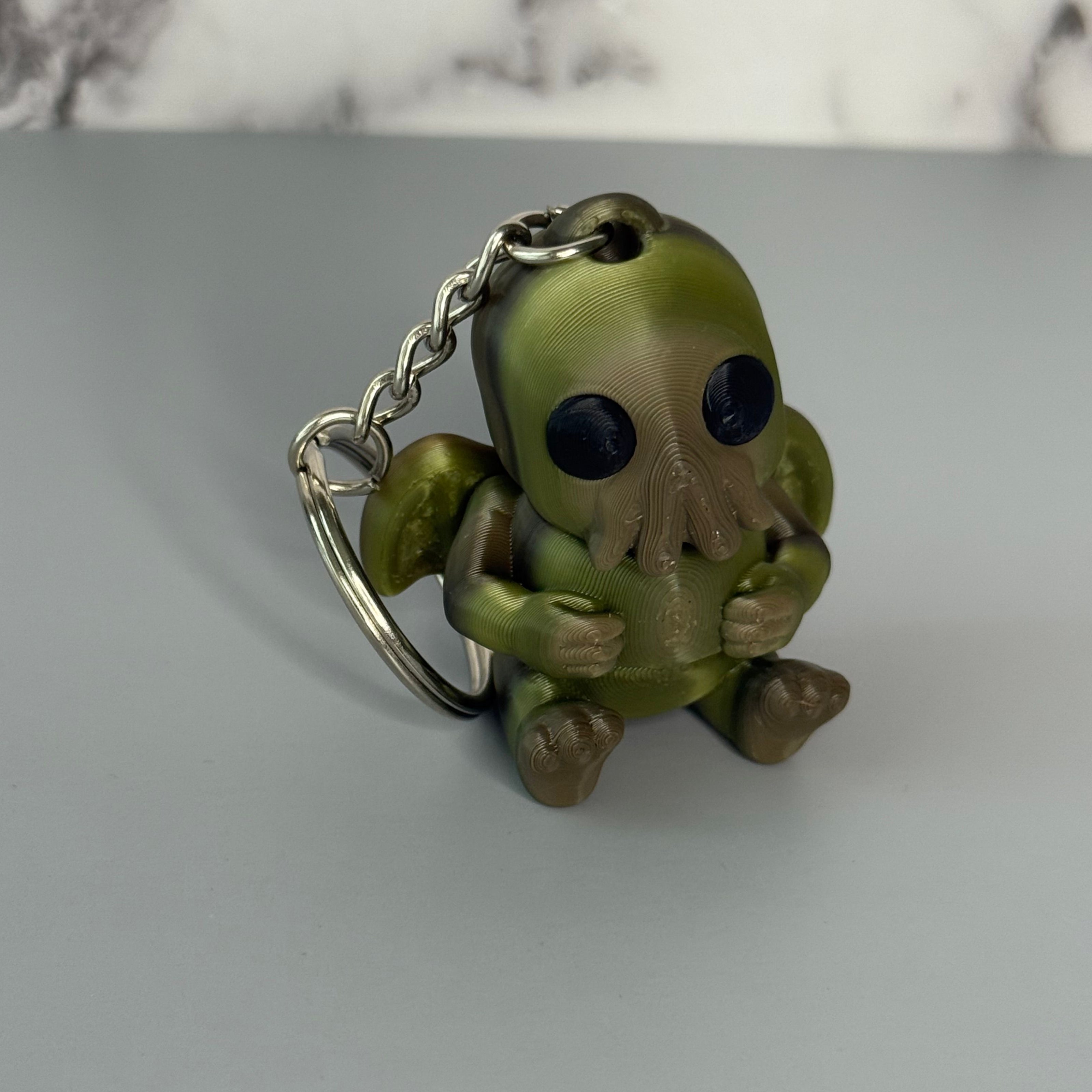 Sitting Cthulhu-shaped keychain figure with wings and face-tentacles on a gray background
