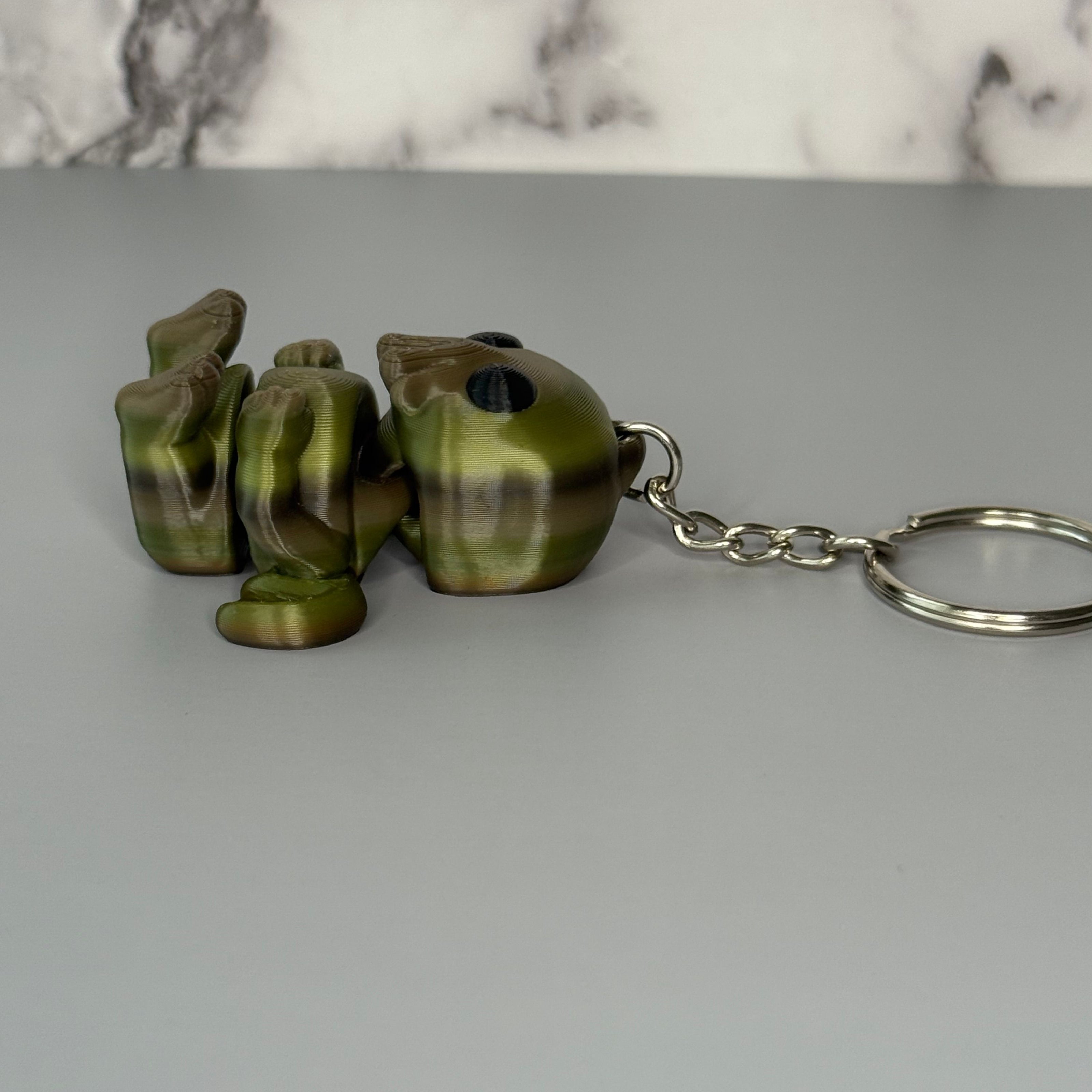 Side of a sitting Cthulhu-shaped keychain figure with wings and face-tentacles on a gray background