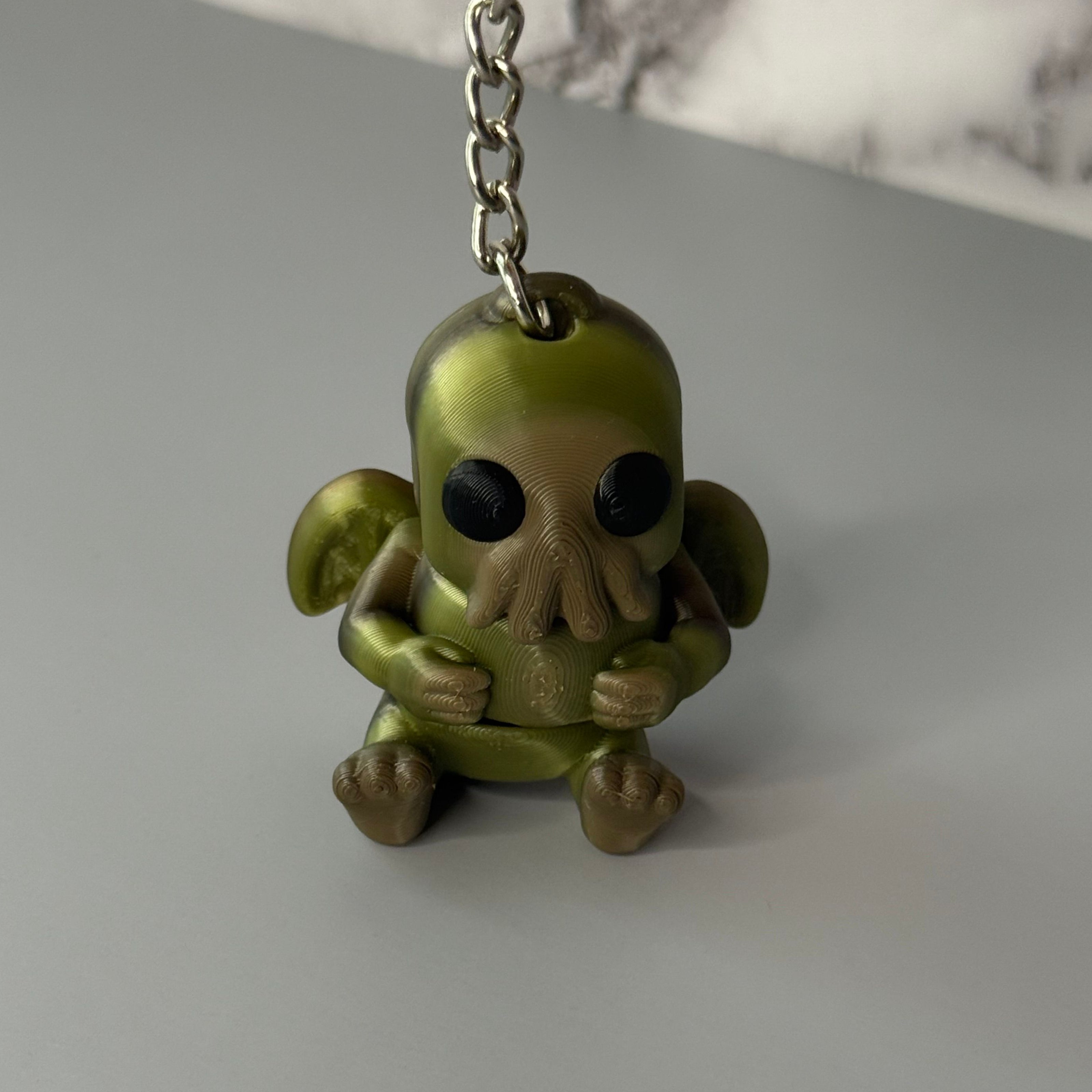 Sitting Cthulhu-shaped keychain figure with wings and face-tentacles on a gray background