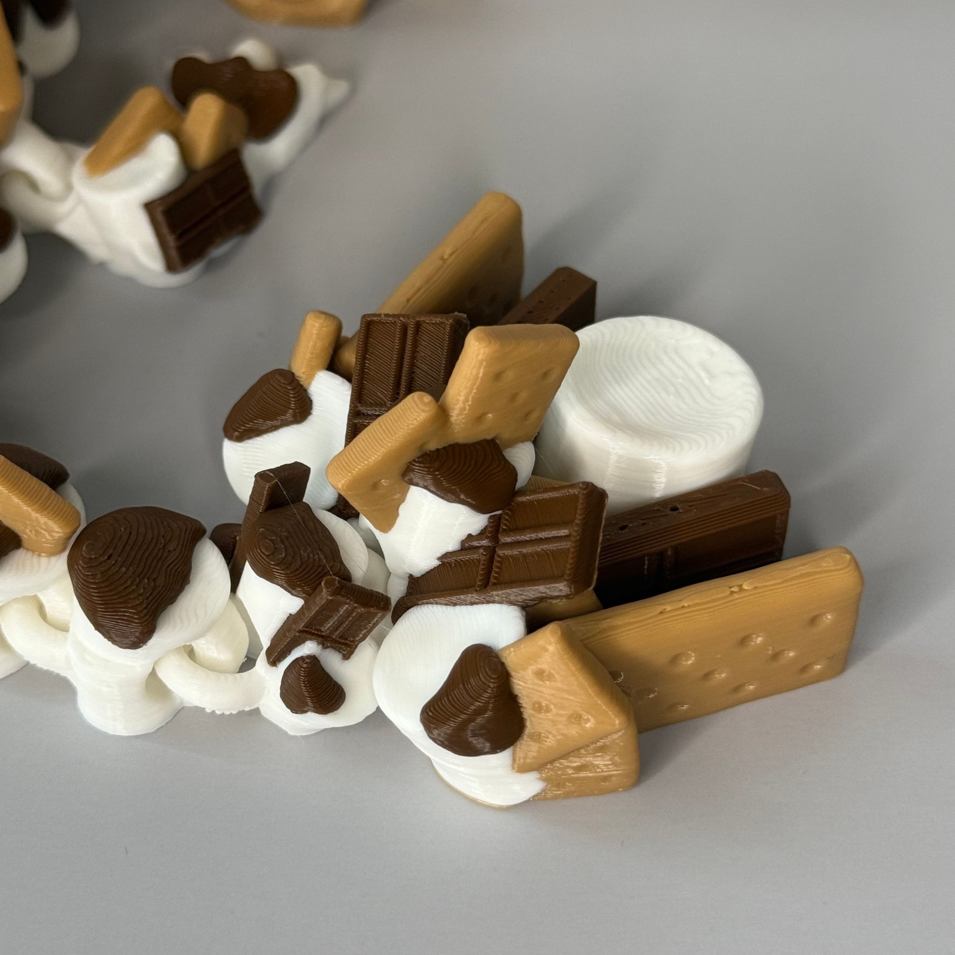 Close-up of dragon tail-shaped toy with s'mores with marshmallows, chocolate bars, and graham crackers on a gray surface.