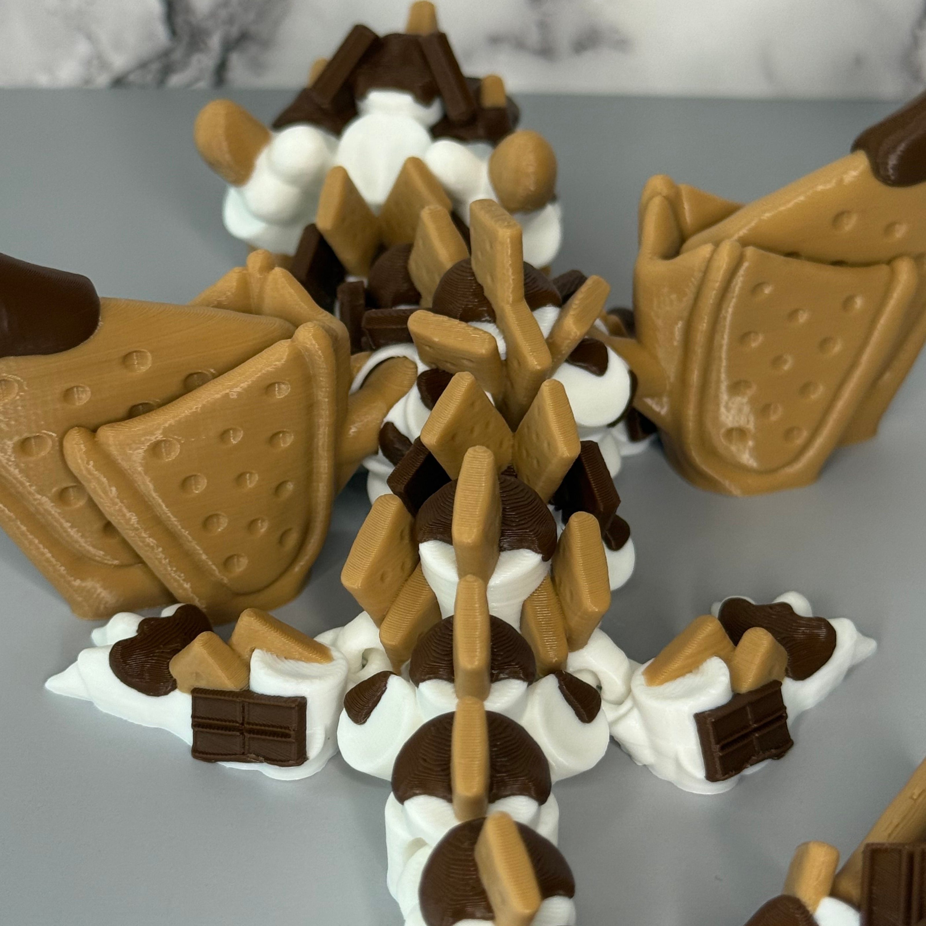 Backside of a toy figure of a dragon with a white, brown, and tan body shaped liked marshmallows, chocolate, and graham crackers on a gray background