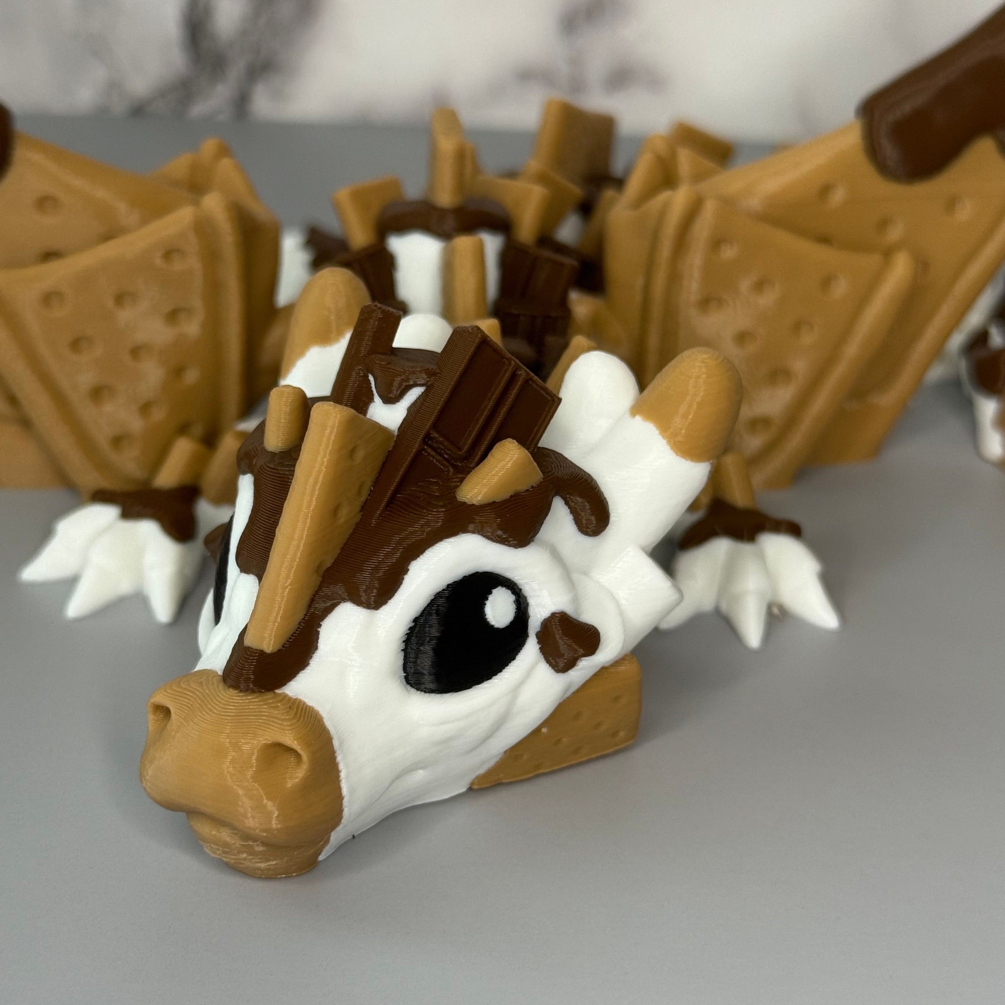 Face of a toy figure of a dragon with a white, brown, and tan body shaped liked chocolate and graham crackers on a gray background