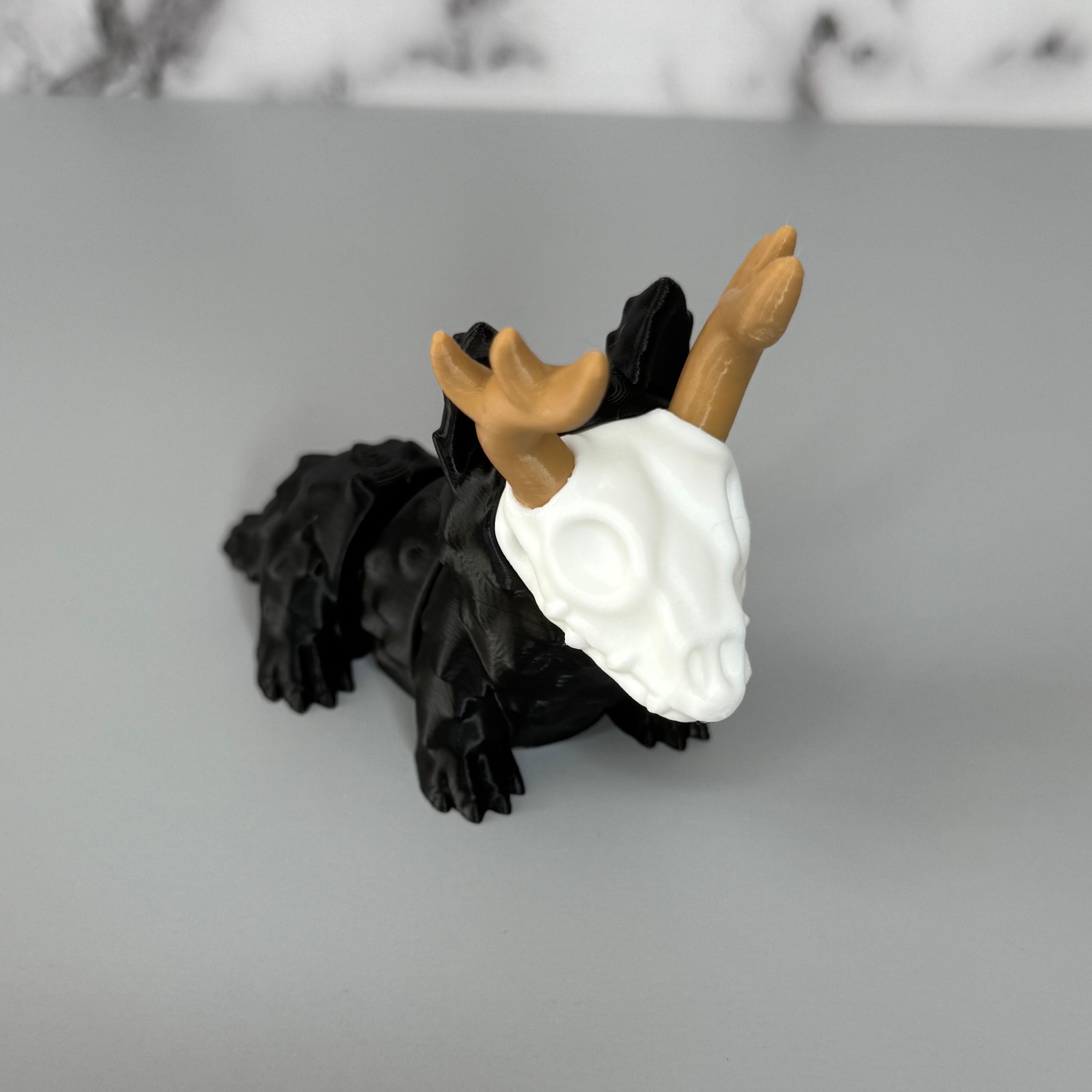Four-legged black animal-shaped figure with antlers and a skull face on a gray background