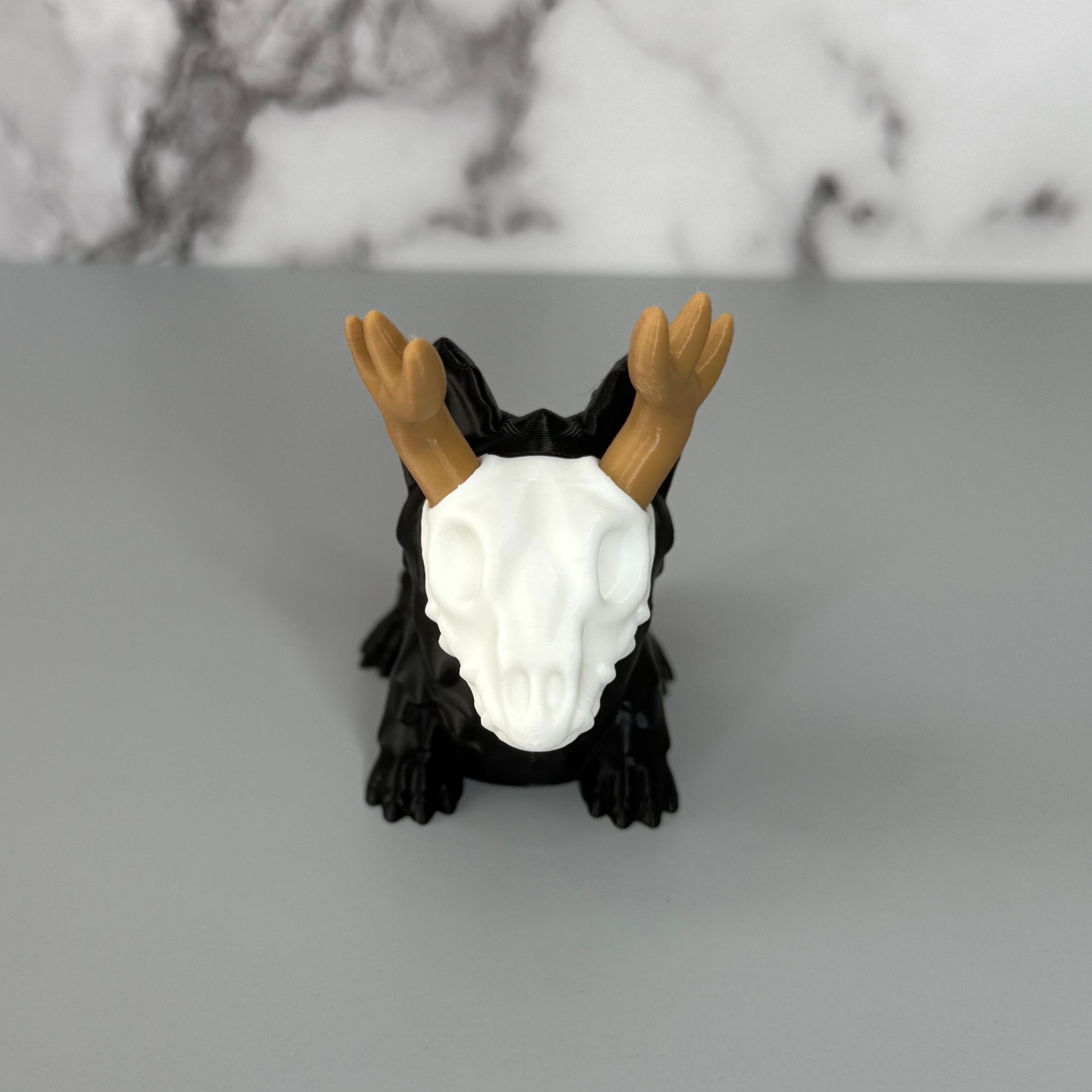 Front of a four-legged black animal-shaped figure with antlers and a skull face on a gray background