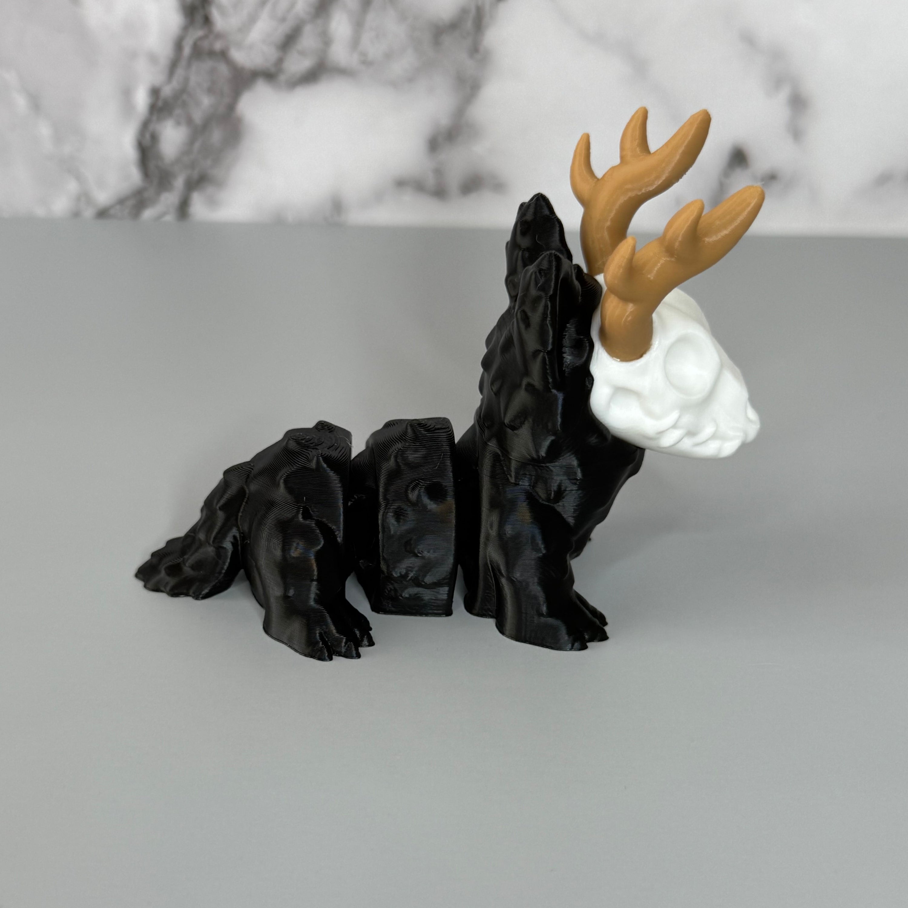 Side of a four-legged black animal-shaped figure with antlers and a skull face on a gray background