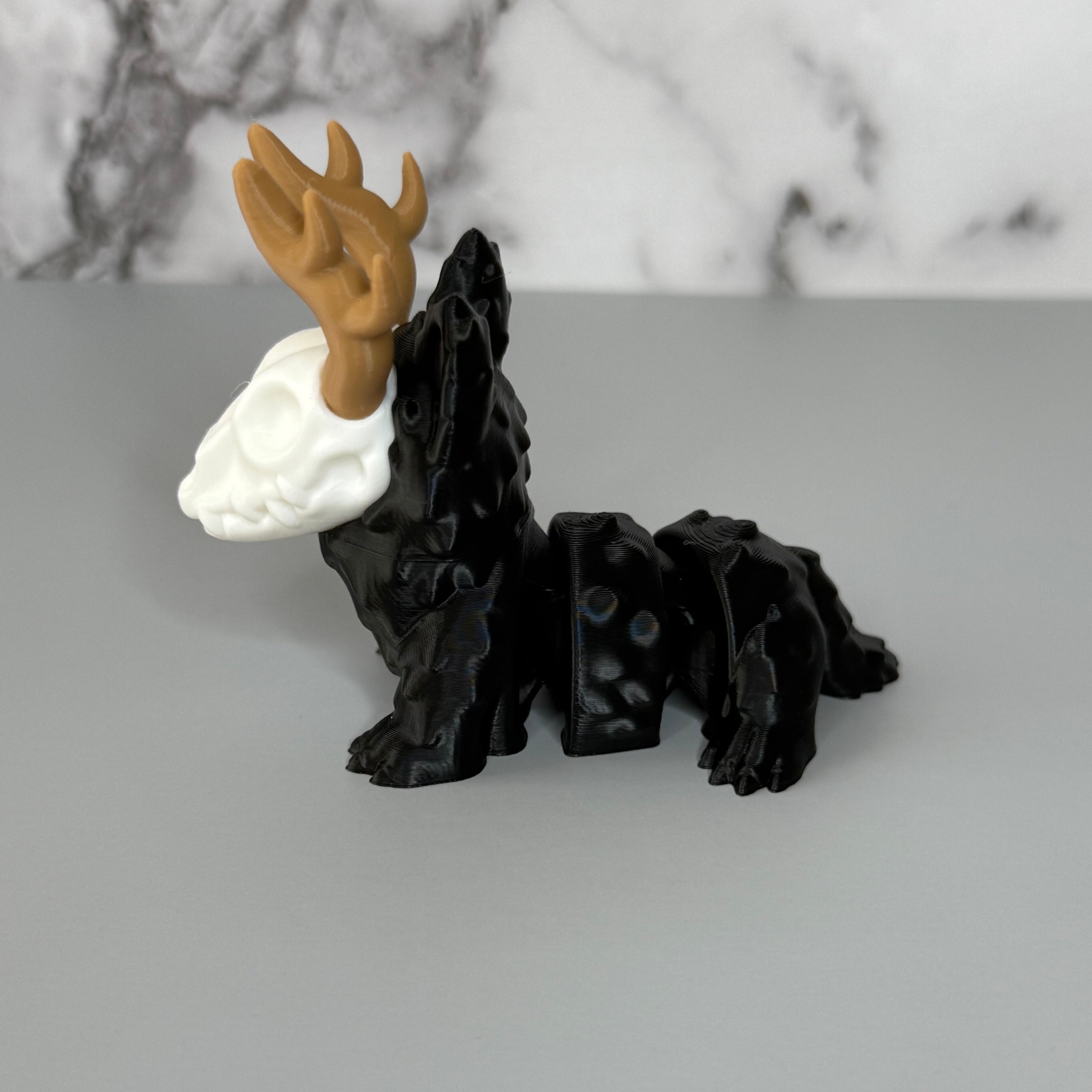 Side of a four-legged black animal-shaped figure with antlers and a skull face on a gray background