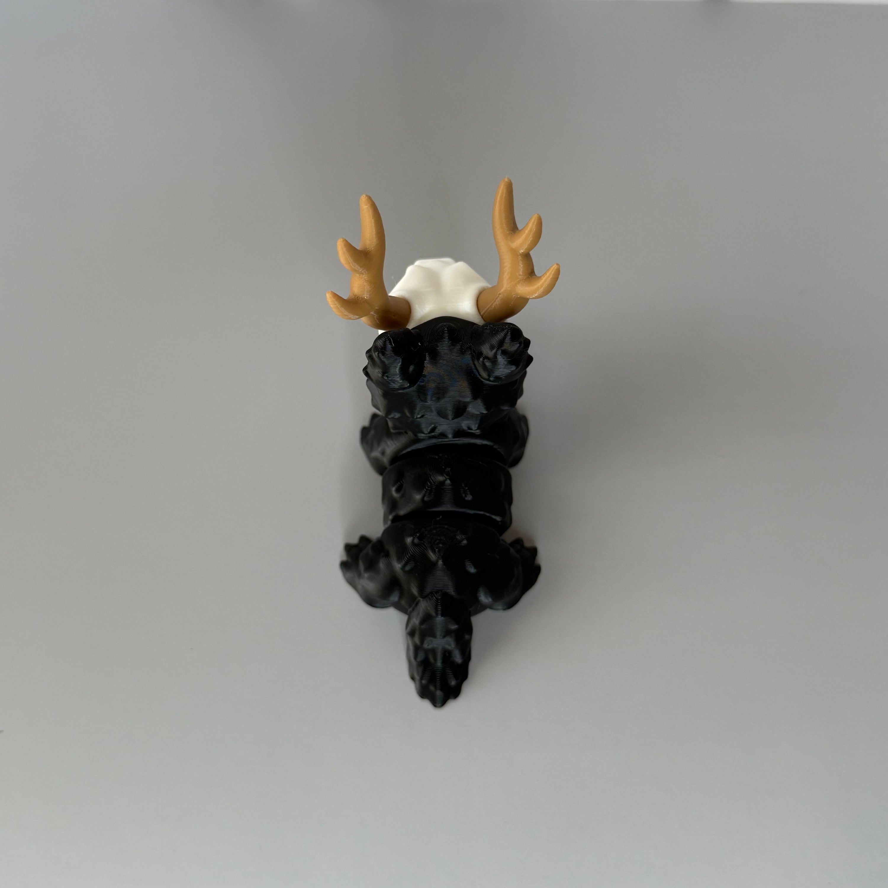 Top of a four-legged black animal-shaped figure with antlers and a skull face on a gray background
