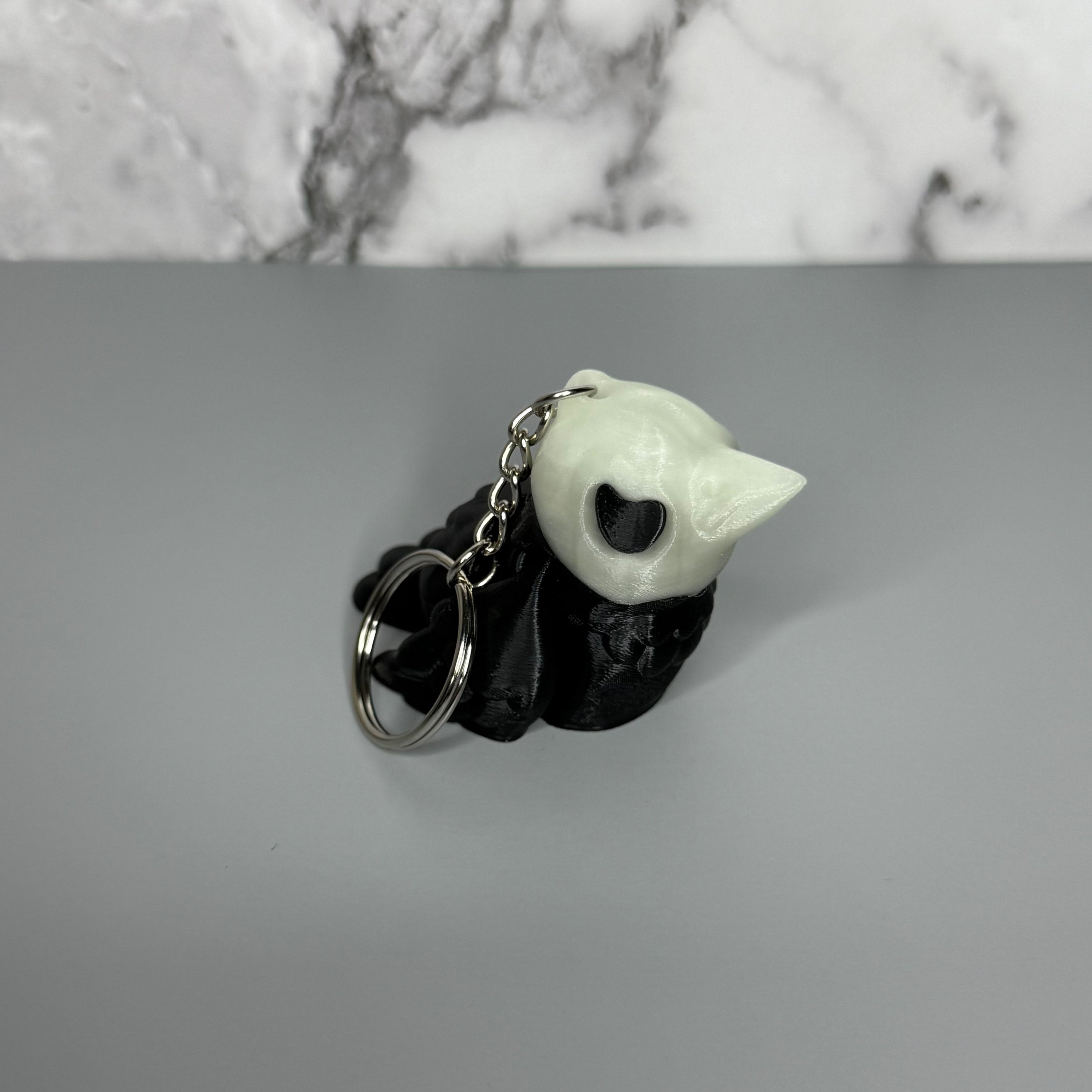 Black and white crow-shaped keychain with crow-shaped skull head on light gray background