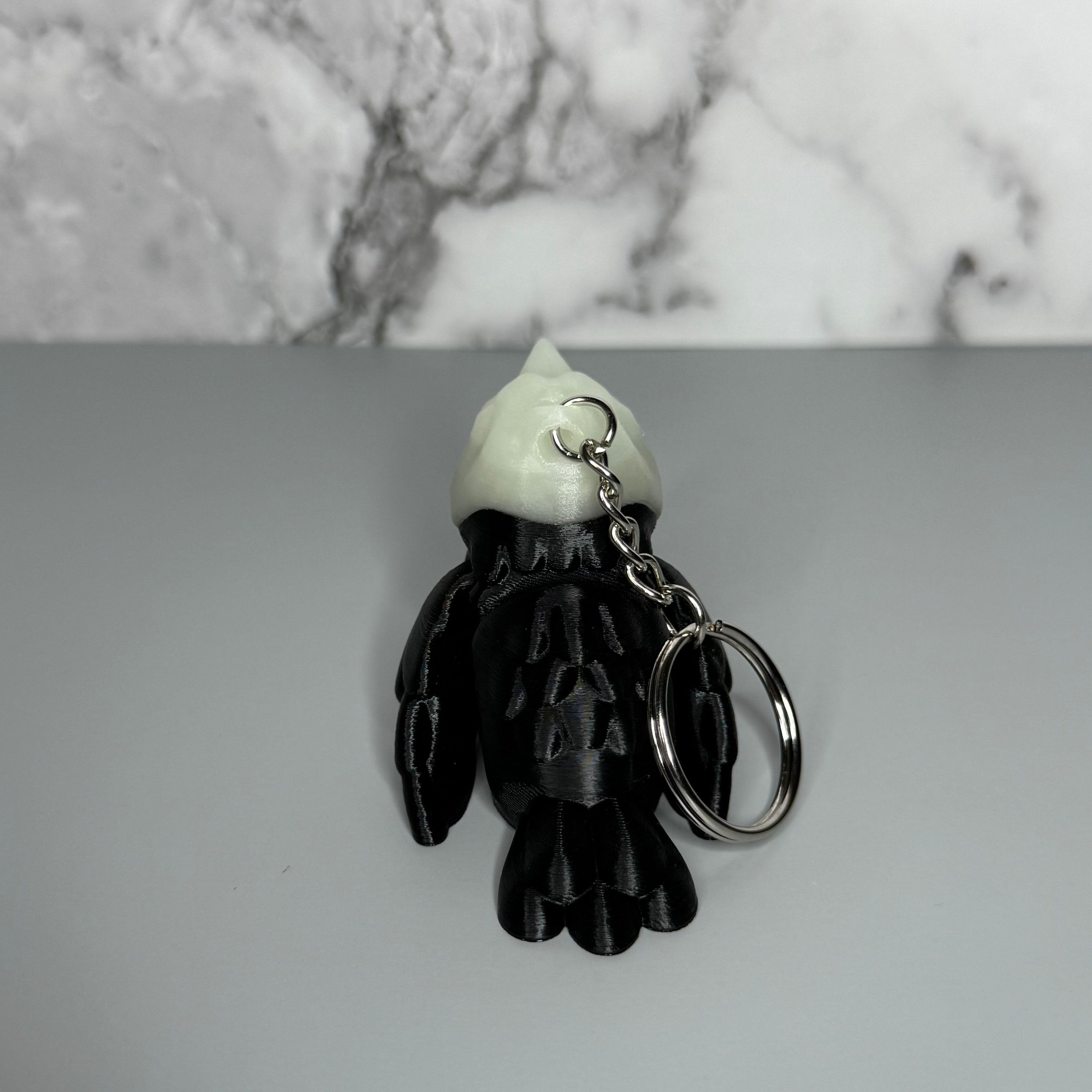 Back side of black and white crow-shaped keychain with crow-shaped skull head on light gray background