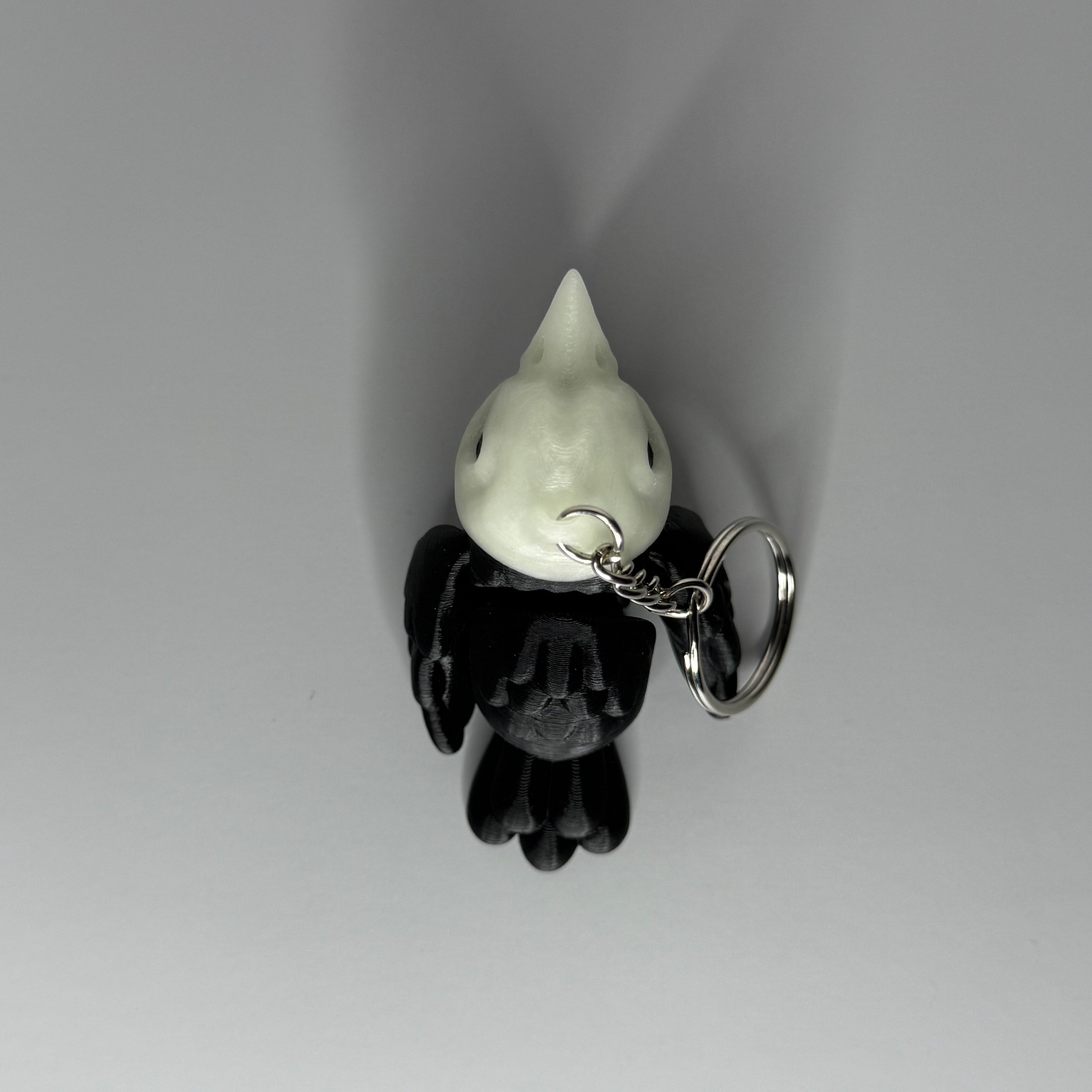 Top side of black and white crow-shaped keychain with crow-shaped skull head on light gray background
